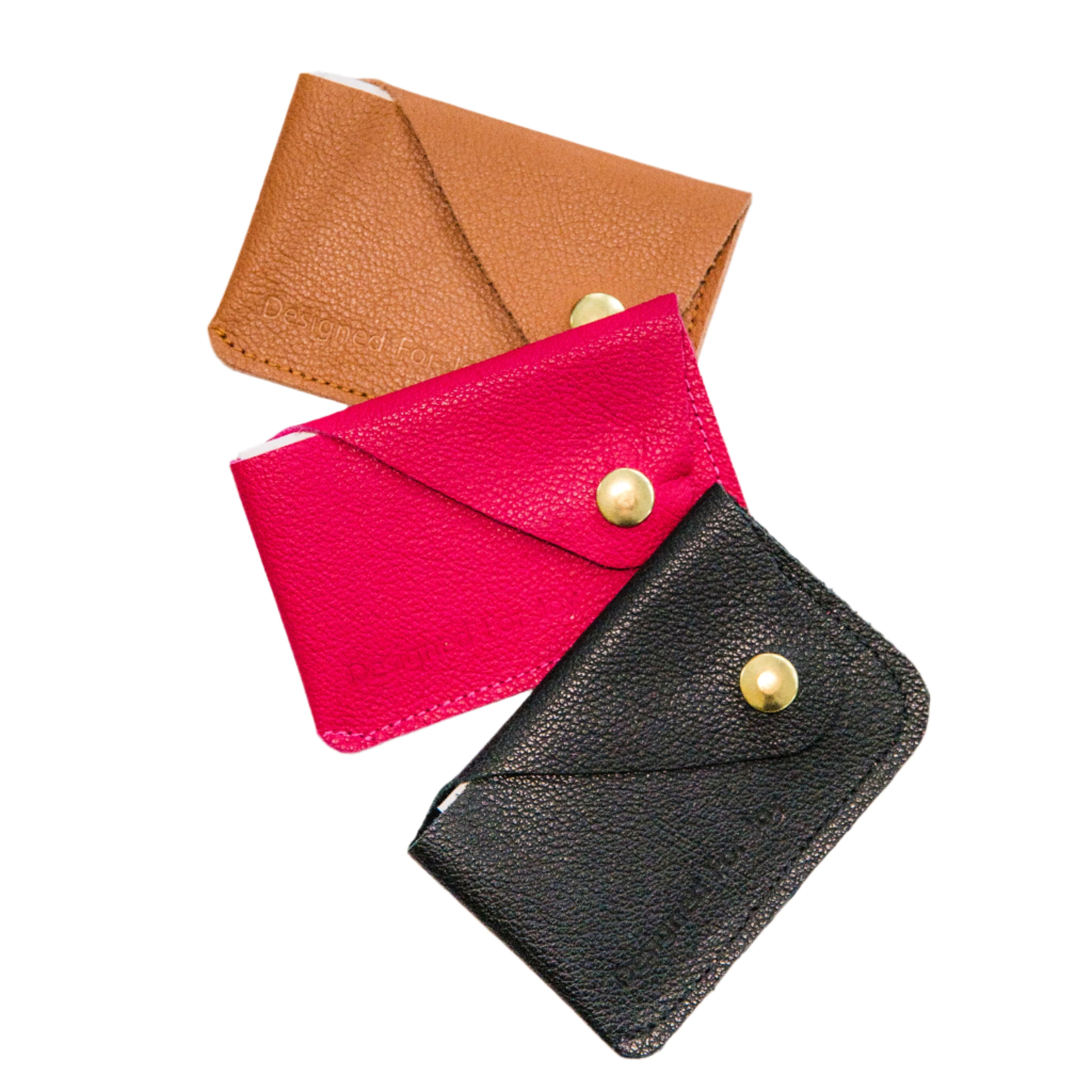 Three leather credit card wallets in caramel brown, pink, and black colors with brass snap closures, on a white background
