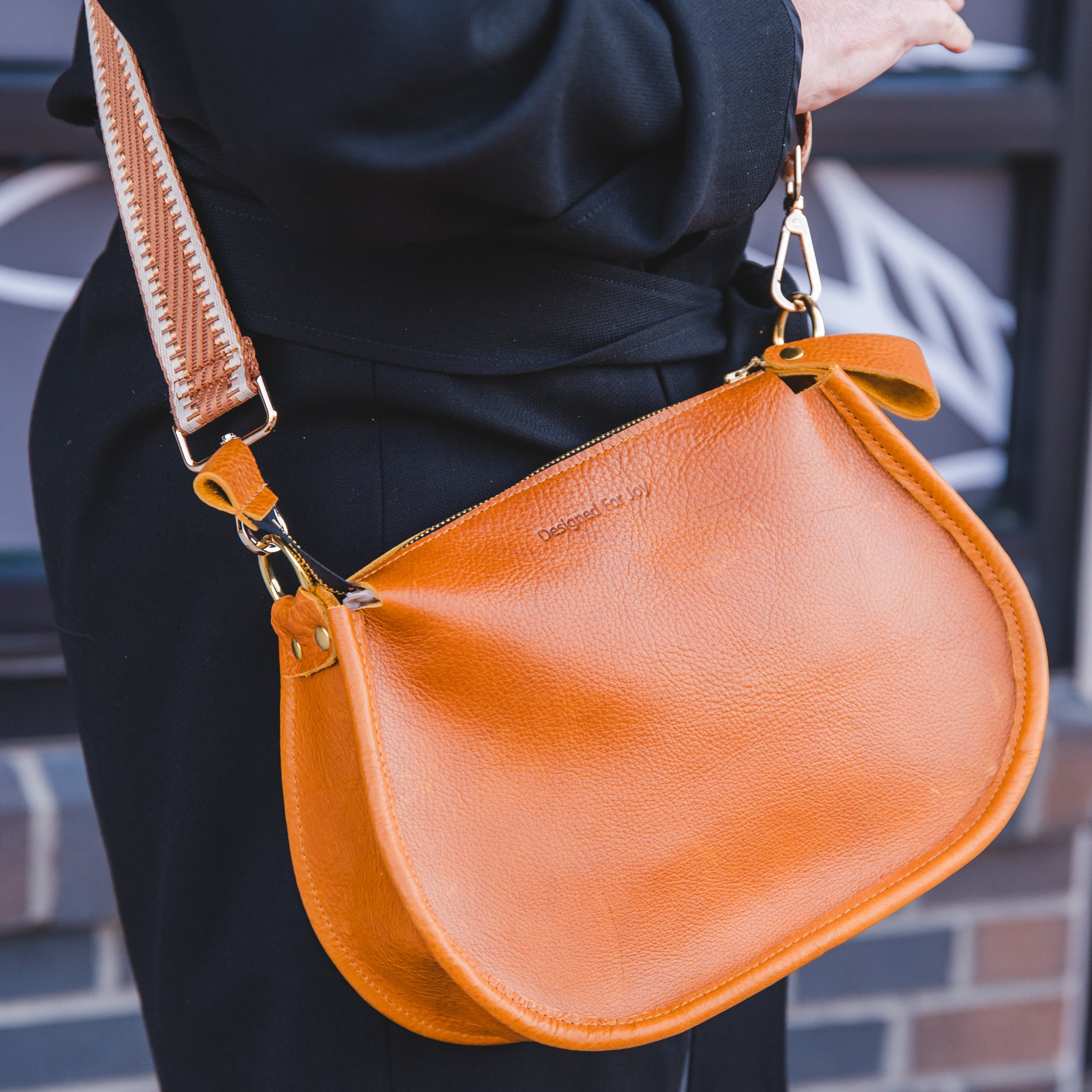 Close up of a person wearing a caramel brown crossbody handbag in an outdoor setting
