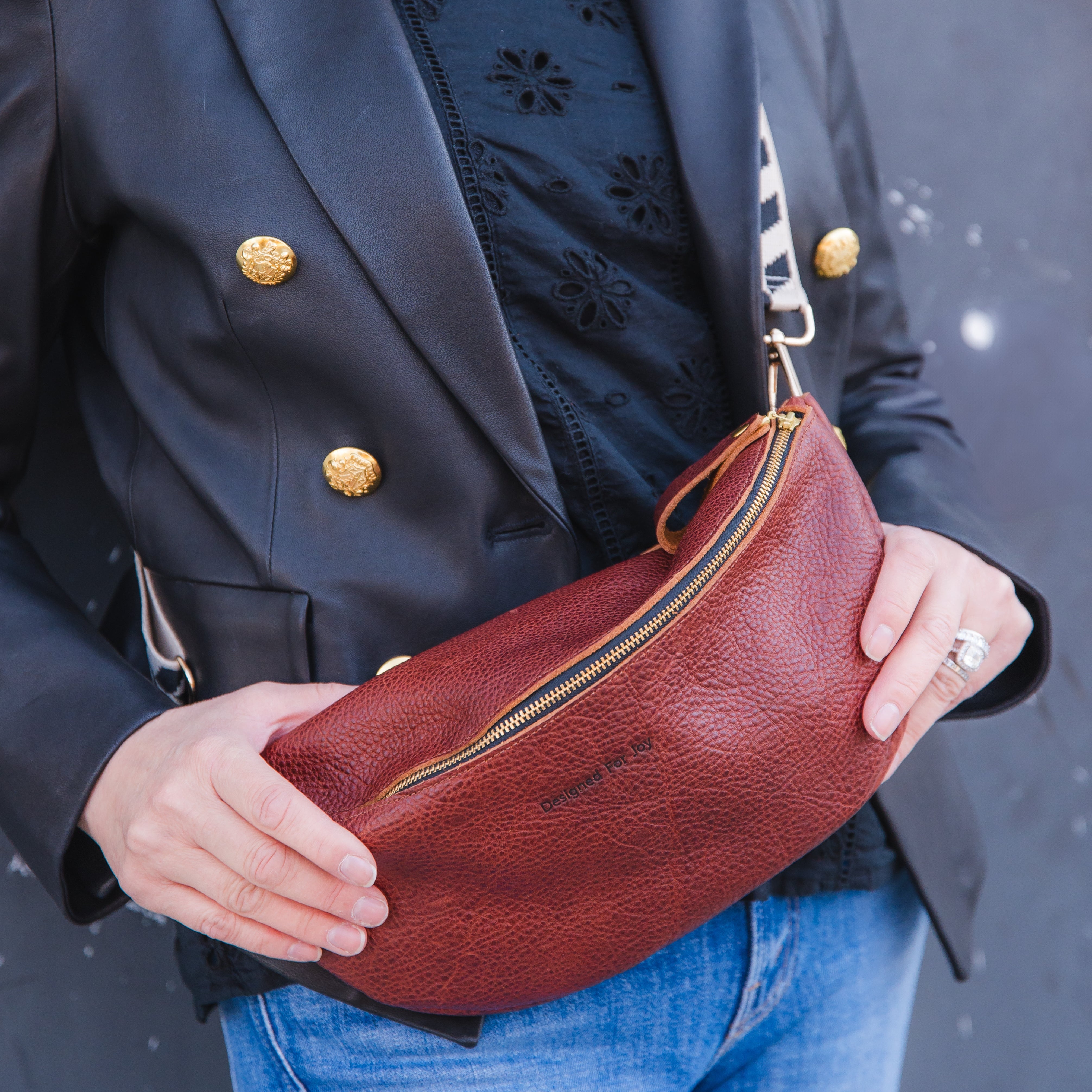 Close up of a person wearing a cinnamon brown crossbody sling handbag while holding it with both hands