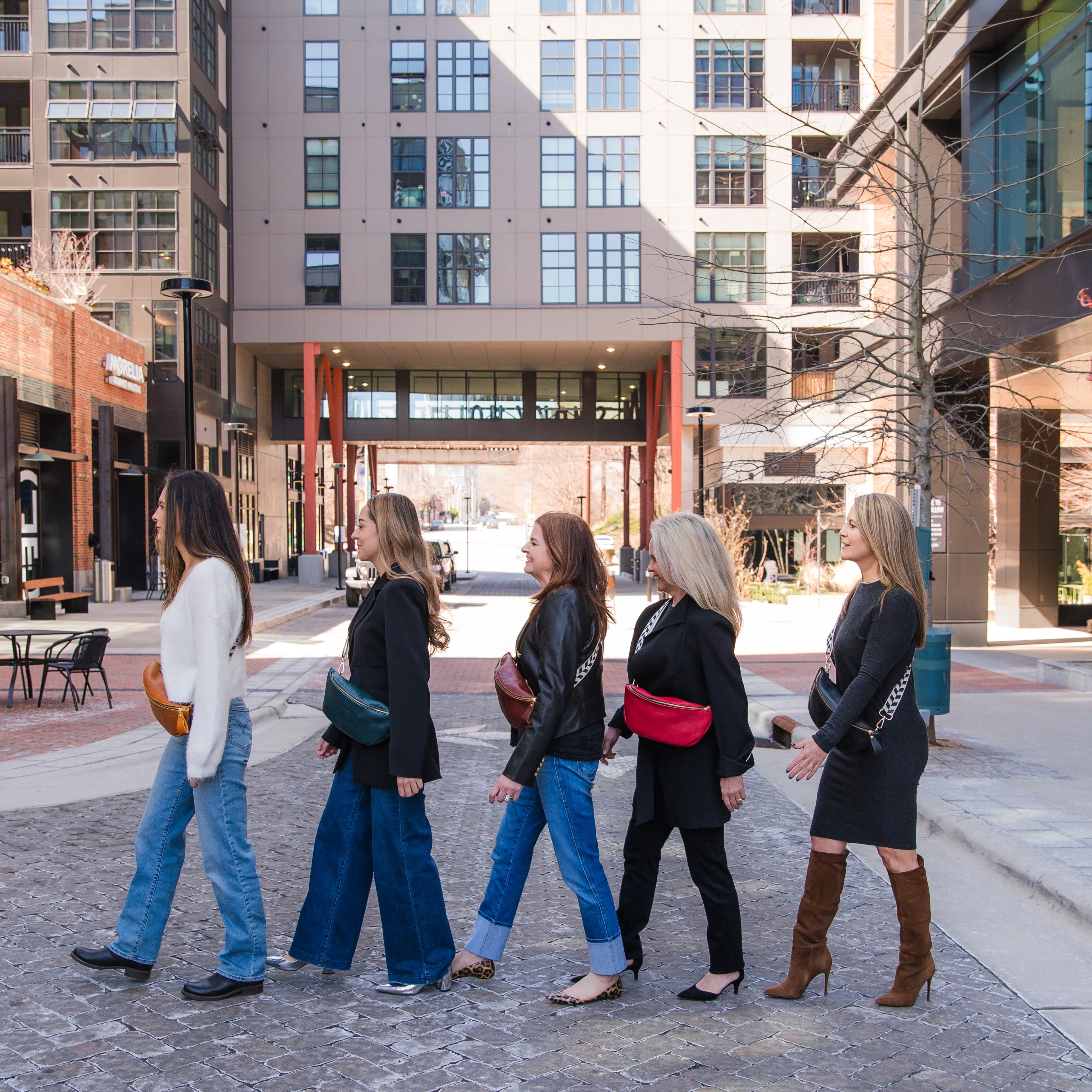 A line of women posing while wearing different colors of the crossbody sling handbag