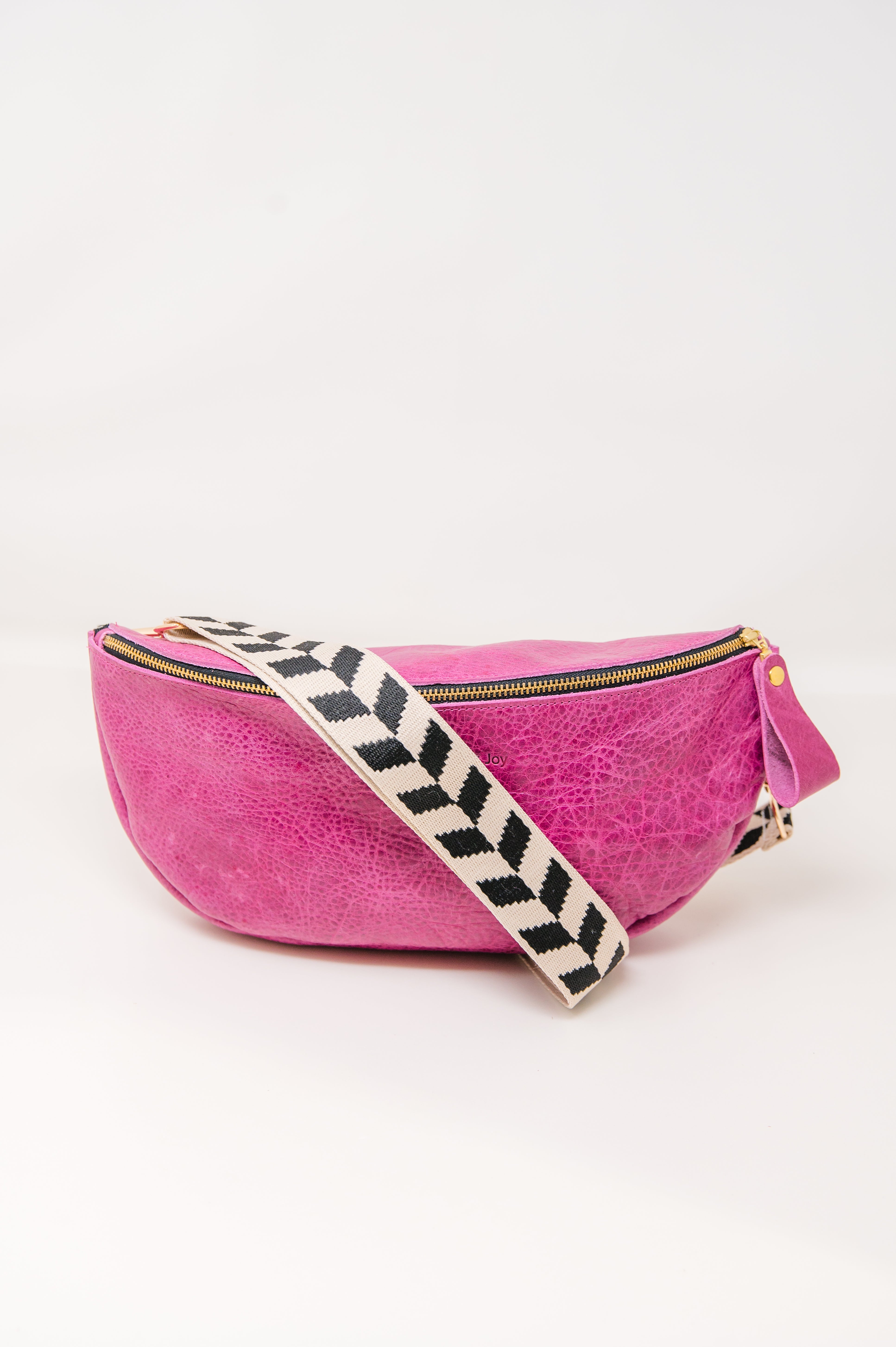 Pink crossbody sling handbag with a black and white geometric patterned strap on a white background
