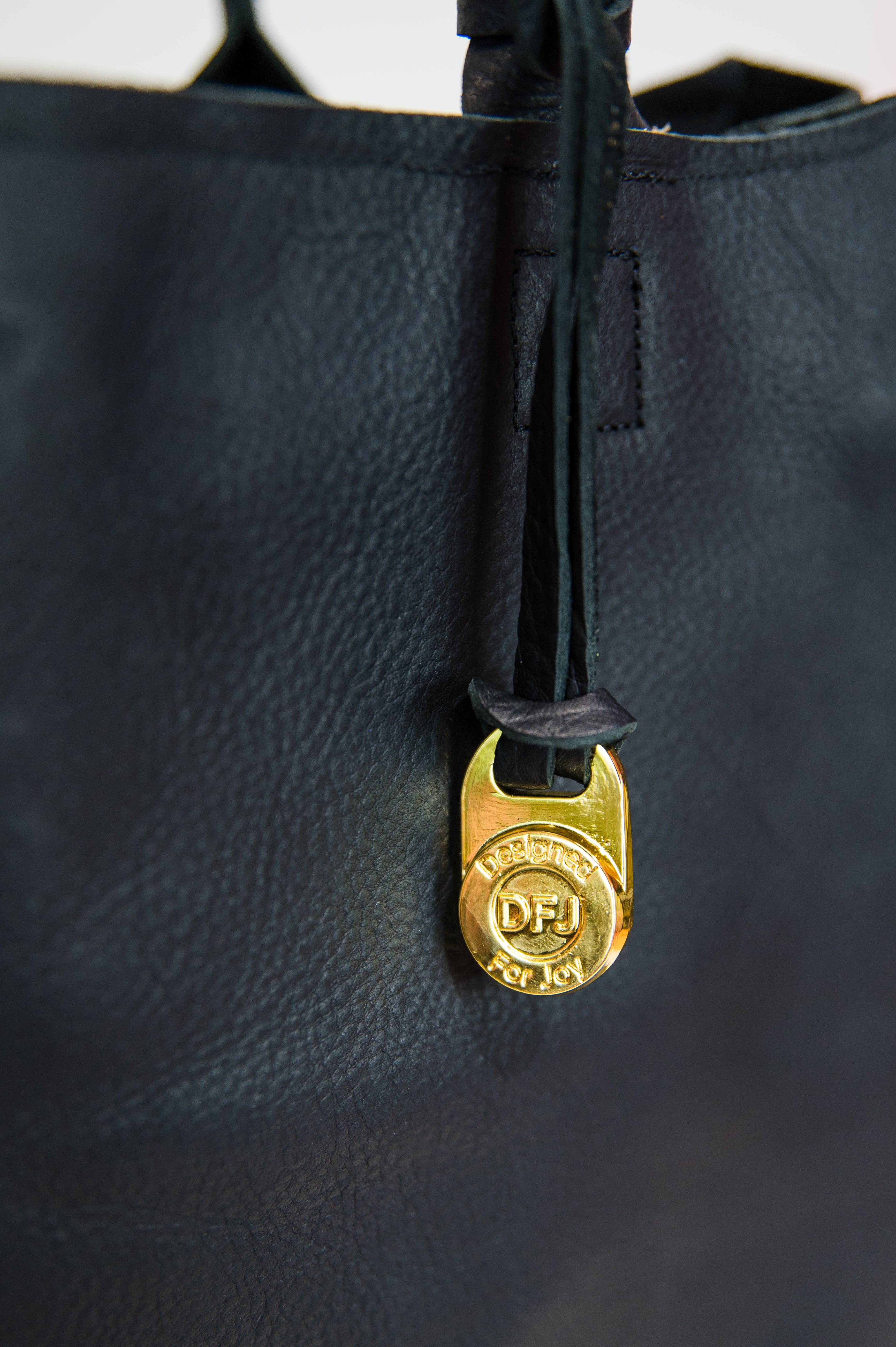 A close-up of the gold "DFJ" charm accessory on a black laptop tote bag