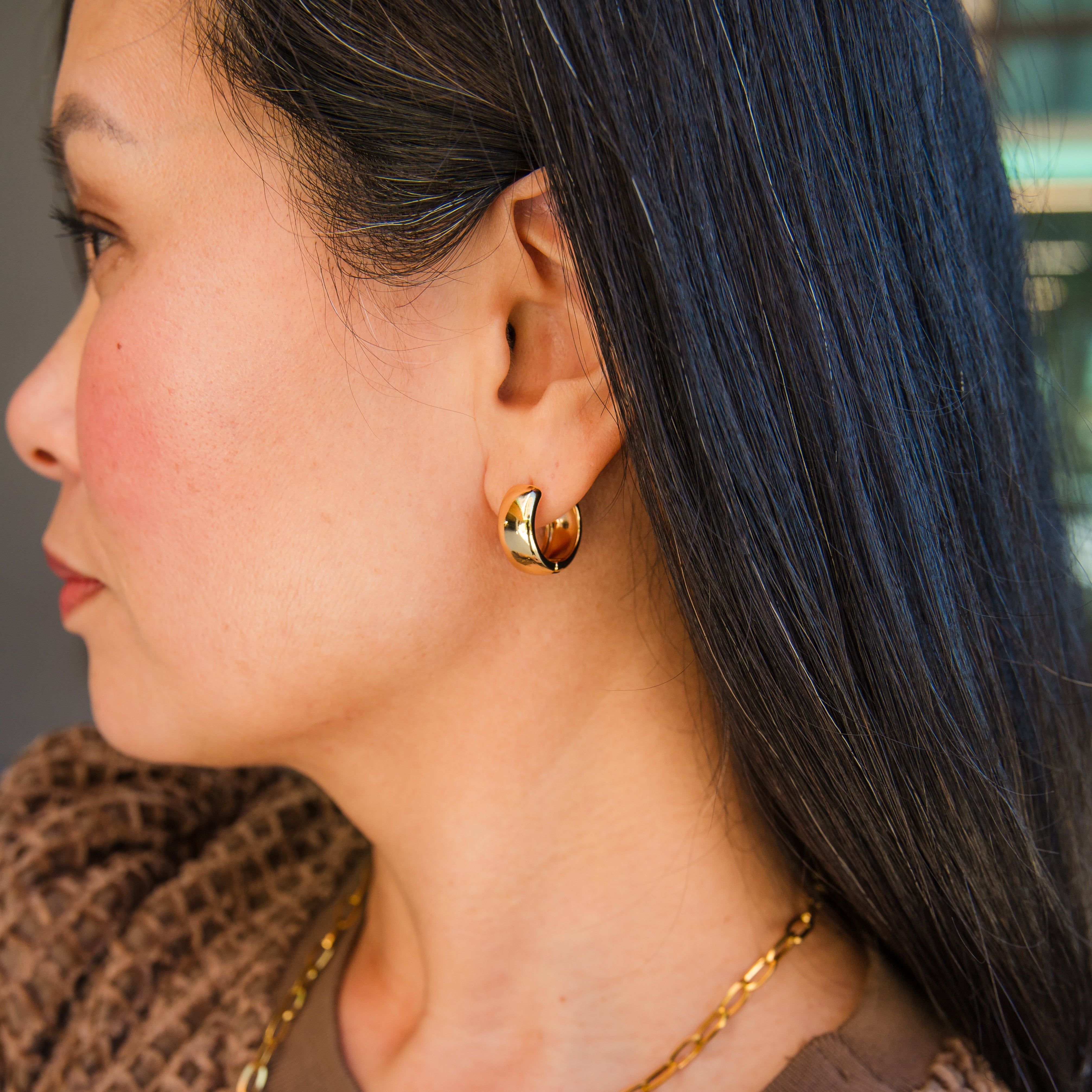 Person wearing a gold-colored wide mini hoop earring