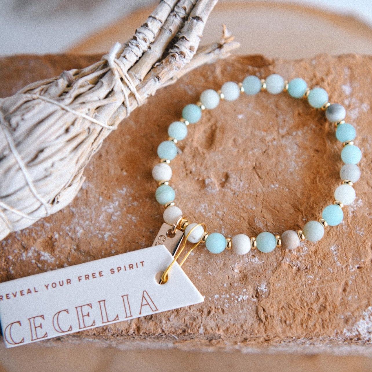 Multicolored amazonite beaded bracelet with gold colored spacer beads, and tags with 'One Tree Planted' and 'Reveal Your Free Spirit Cecelia' text, displayed on a stone surface