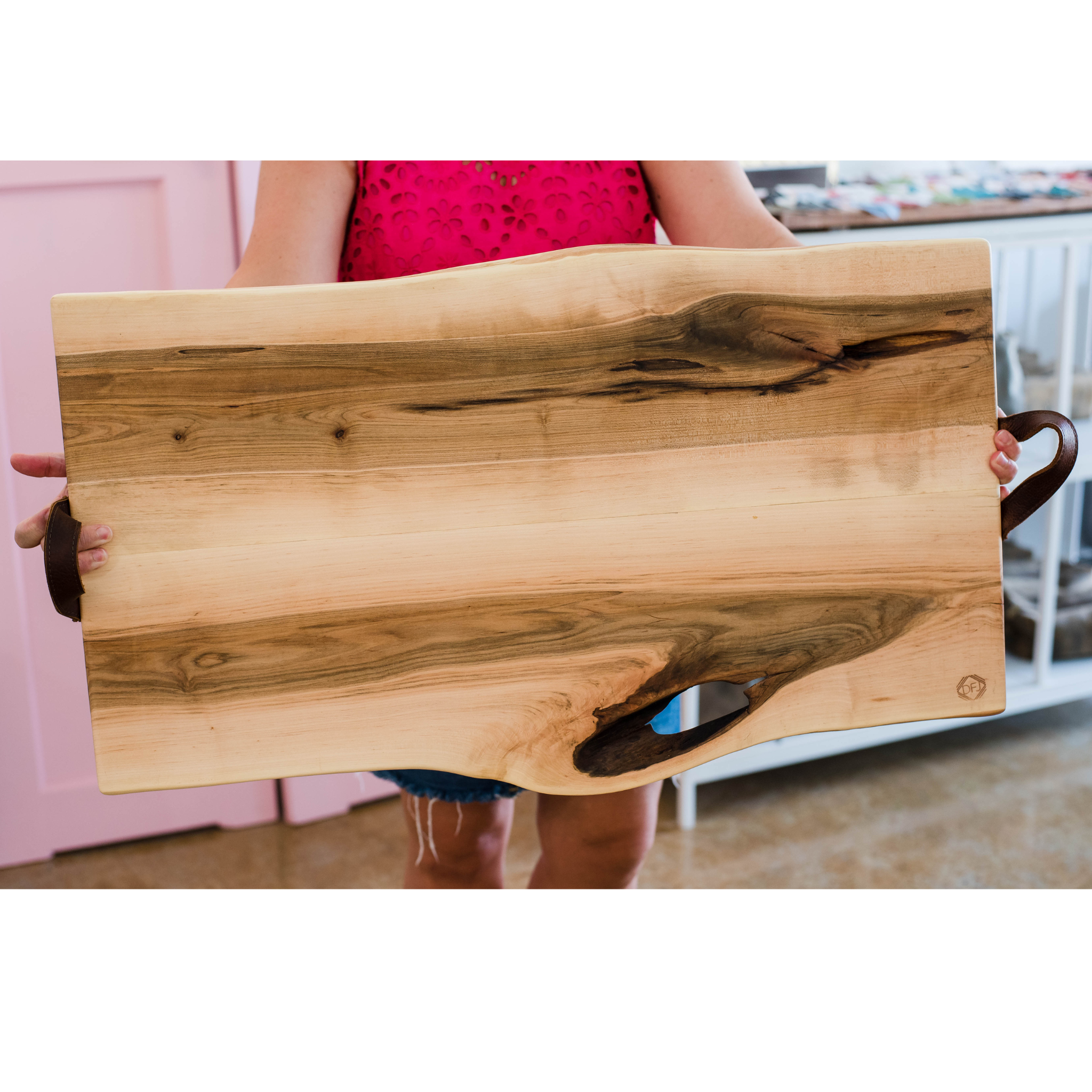 A person holding a live-edge charcuterie board made of maple wood with leather handles