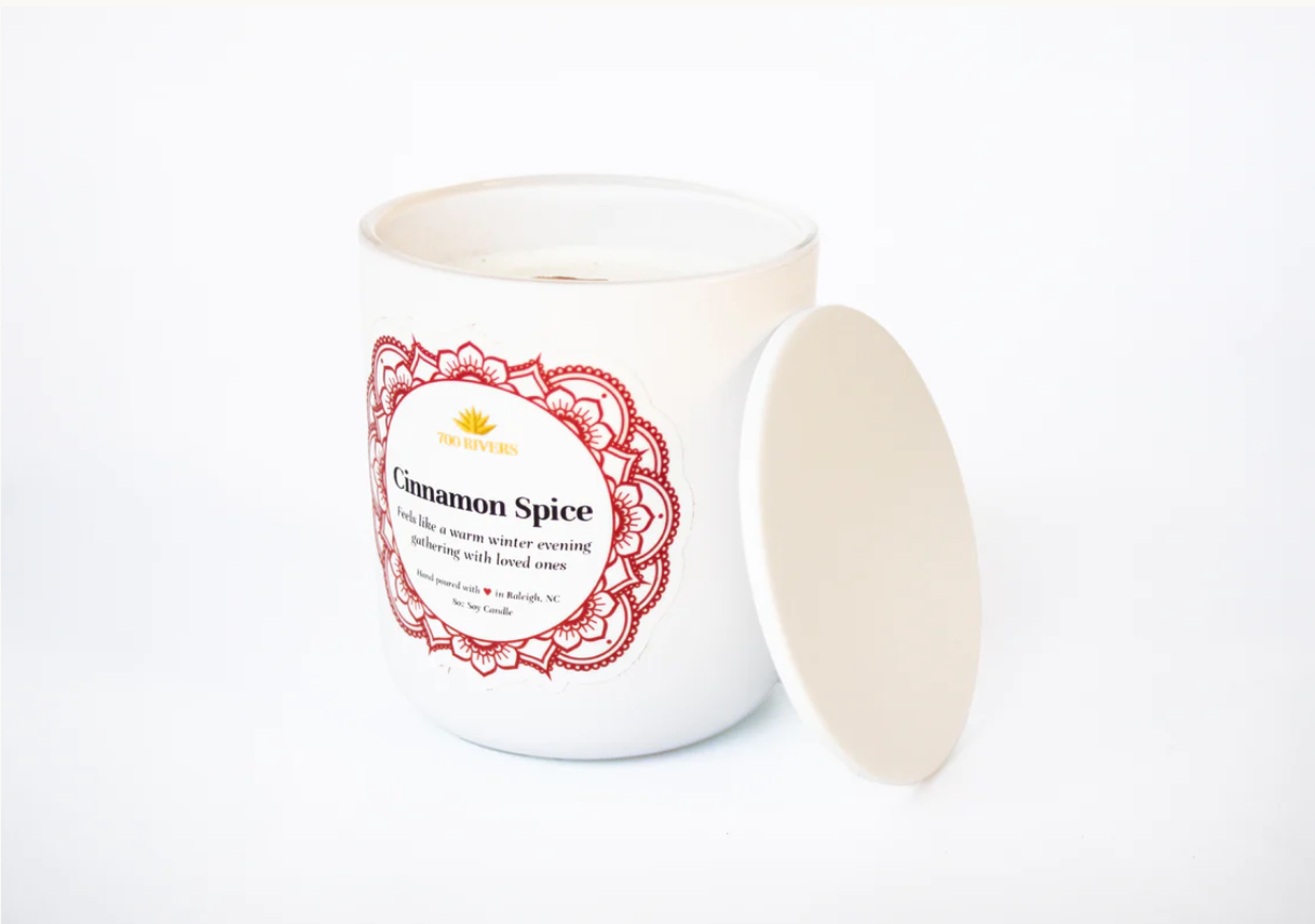 White candle with a wooden wick labeled 'Cinnamon Spice' with red floral designs