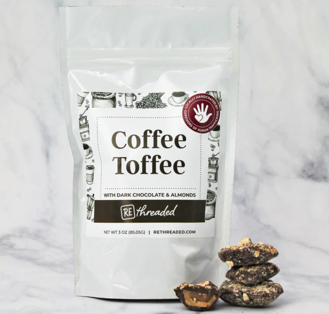 A white bag labeled 'Coffee Toffee With Dark Chocolate & Almonds', displayed alongside pieces of toffee on a marble background