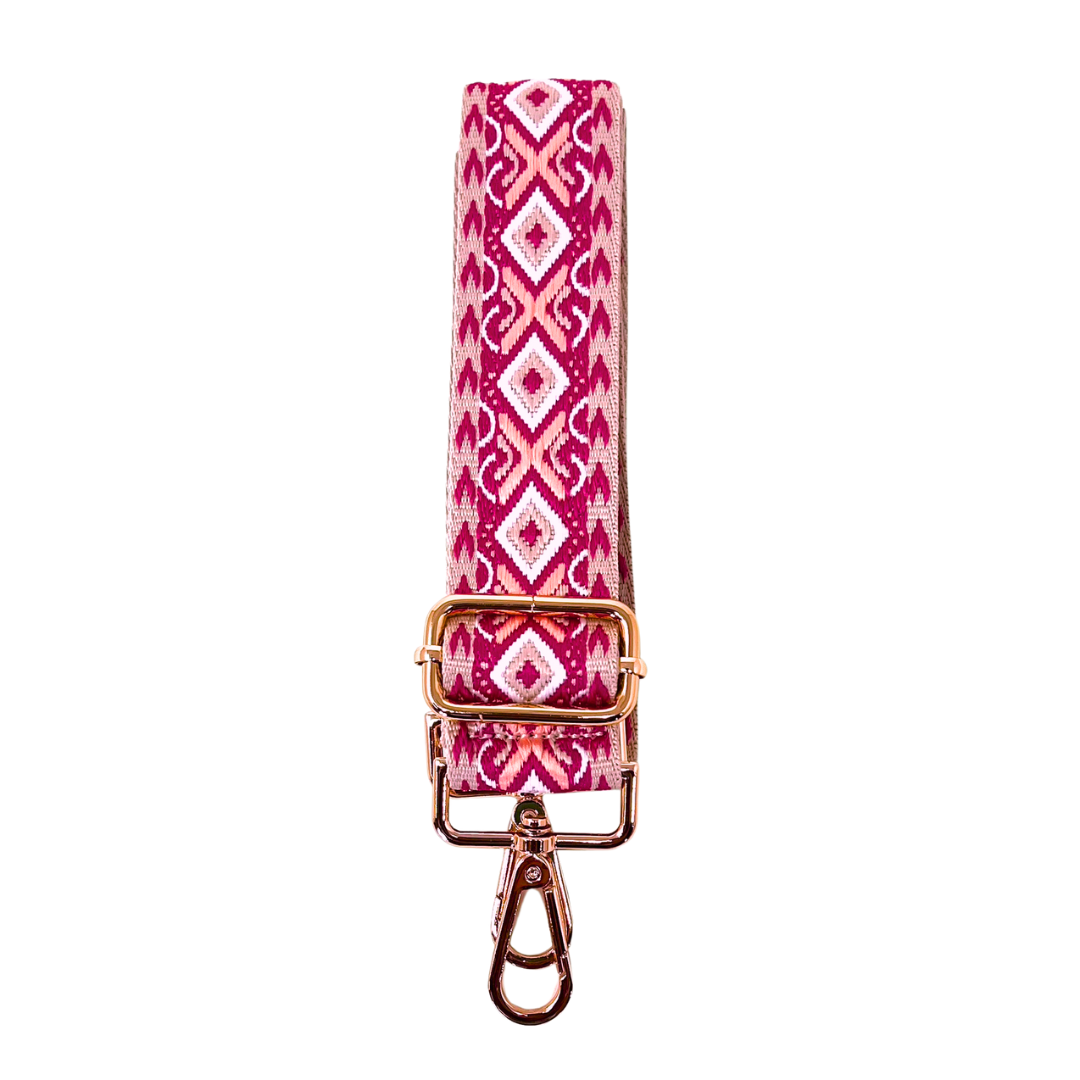 A pink geo-patterned crossbody strap with goldtone hardware, displayed on a white background