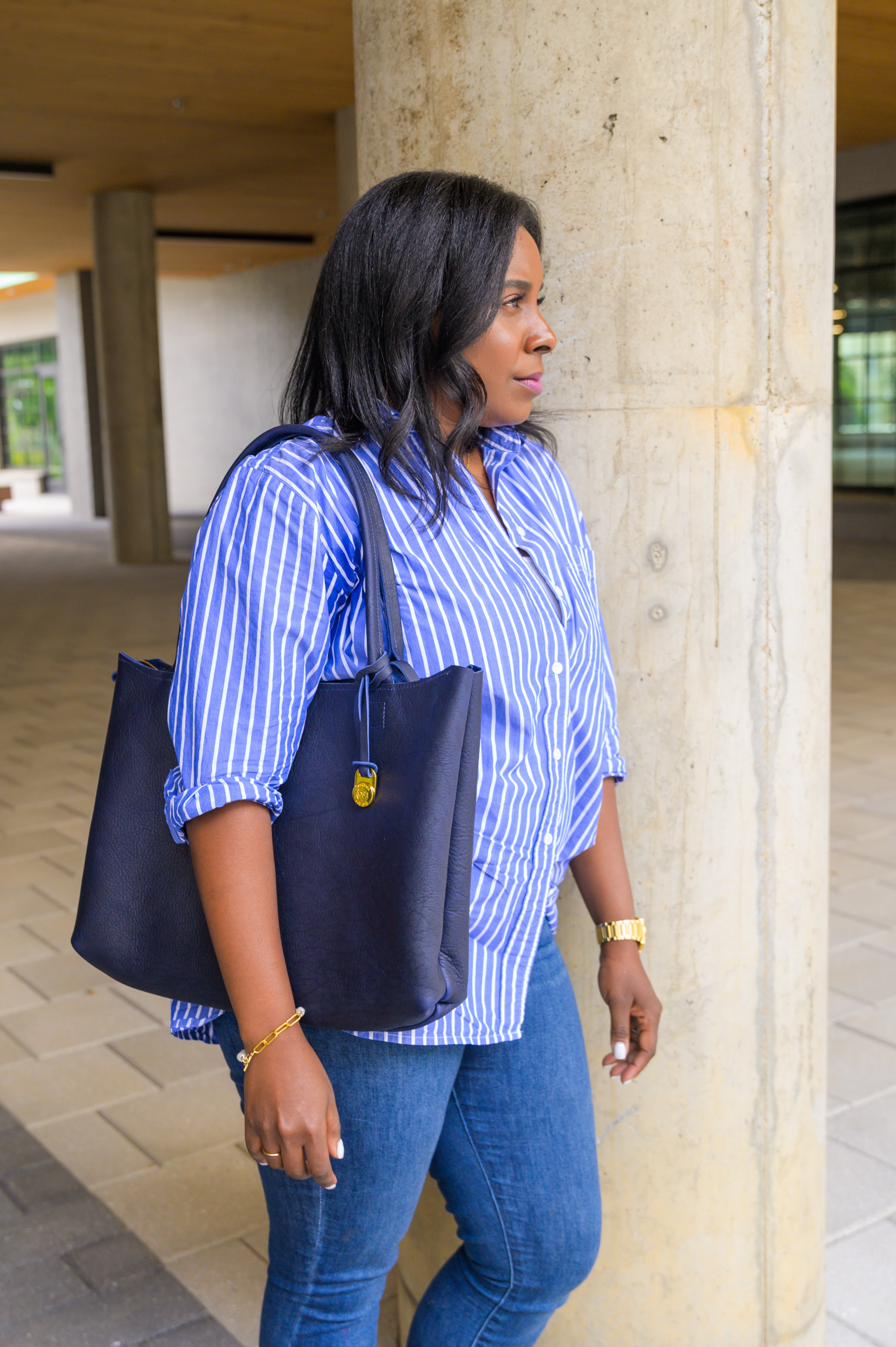 Side angle of a person wearing a navy blue laptop tote bag while learning against a column