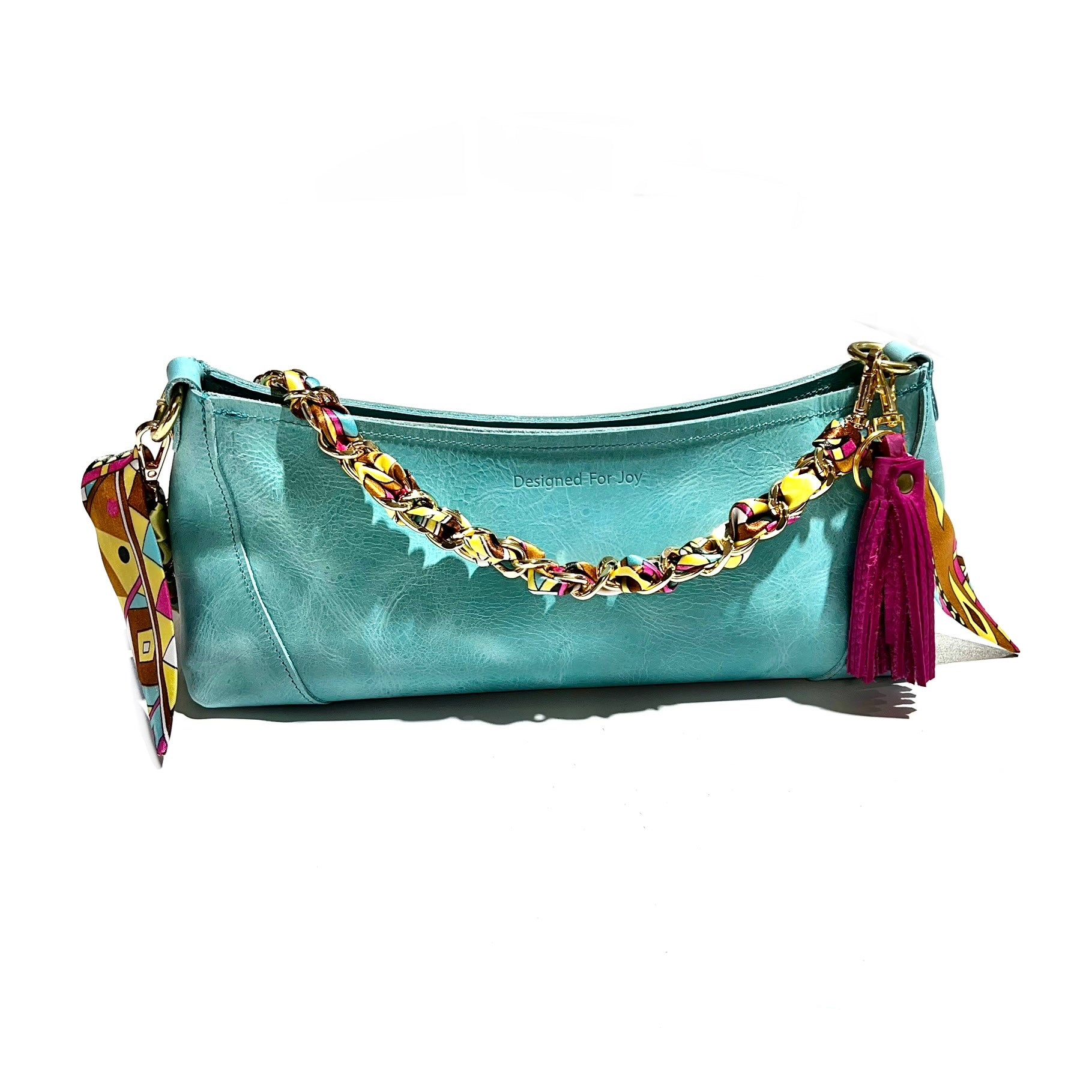 Pink leather tassel keychain attached to a teal blue handbag with a scarf chain strap, displayed on a white background