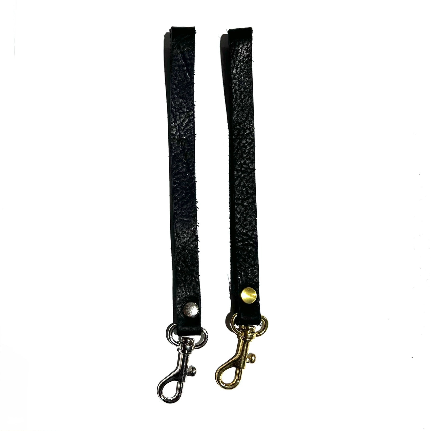 Two black leather wristlet straps, one with a brass clip attachment and the other with a silver clip, displayed on a white background