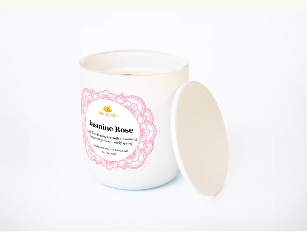 White candle with a wooden wick labeled 'Jasmine Rose' with pink floral designs