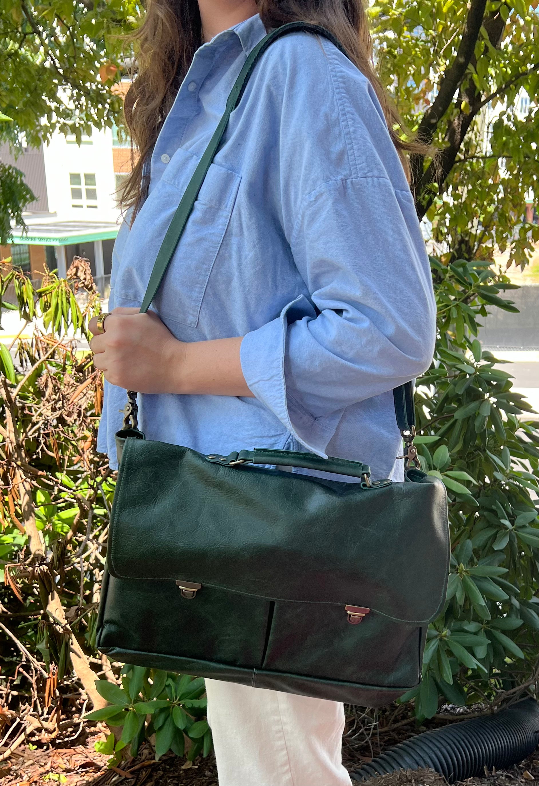 Person carrying a dark green professional messenger/laptop bag in an outdoor setting
