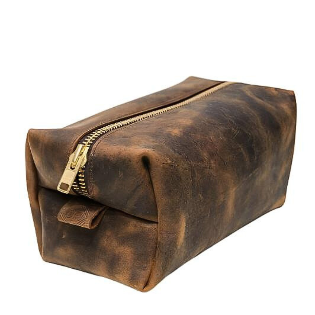 A brown leather dopp bag with a large brass zipper, crafted from slightly oiled leather that shows creases and wrinkles, displayed on a white background