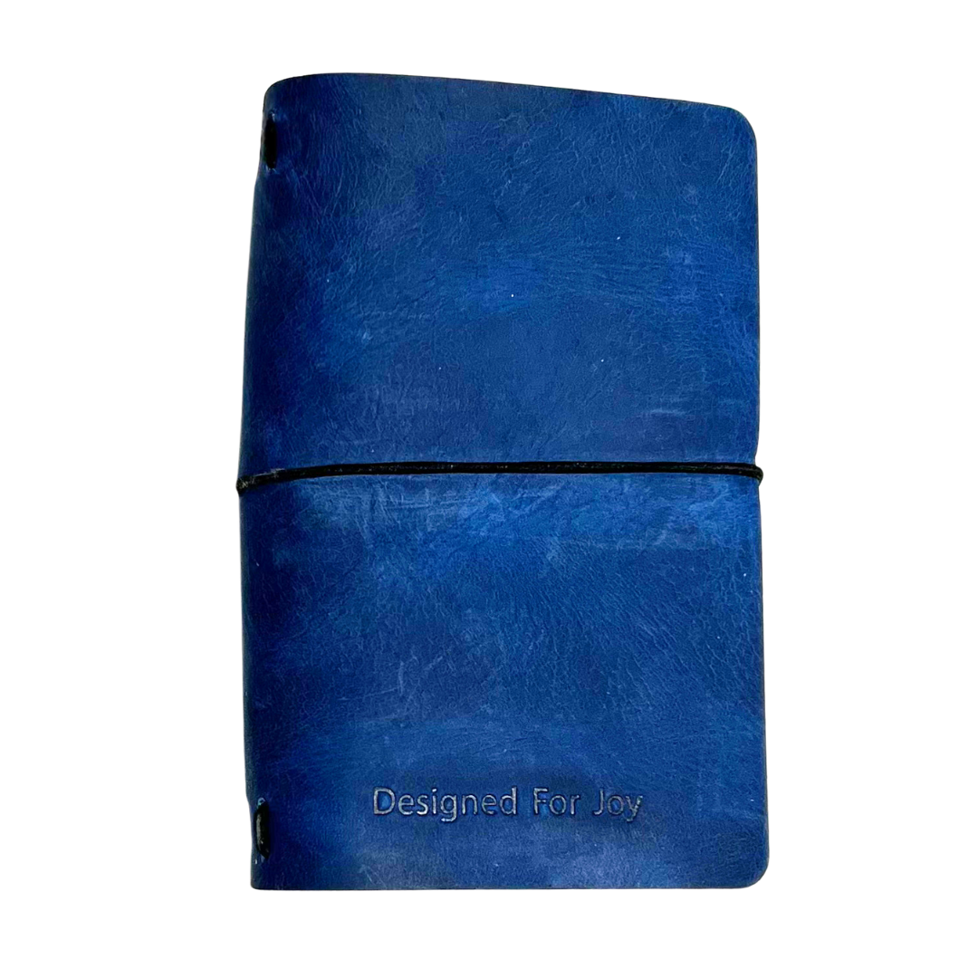 Dark blue notebook with 'Designed for Joy' text on the cover and a black strap, on a white background