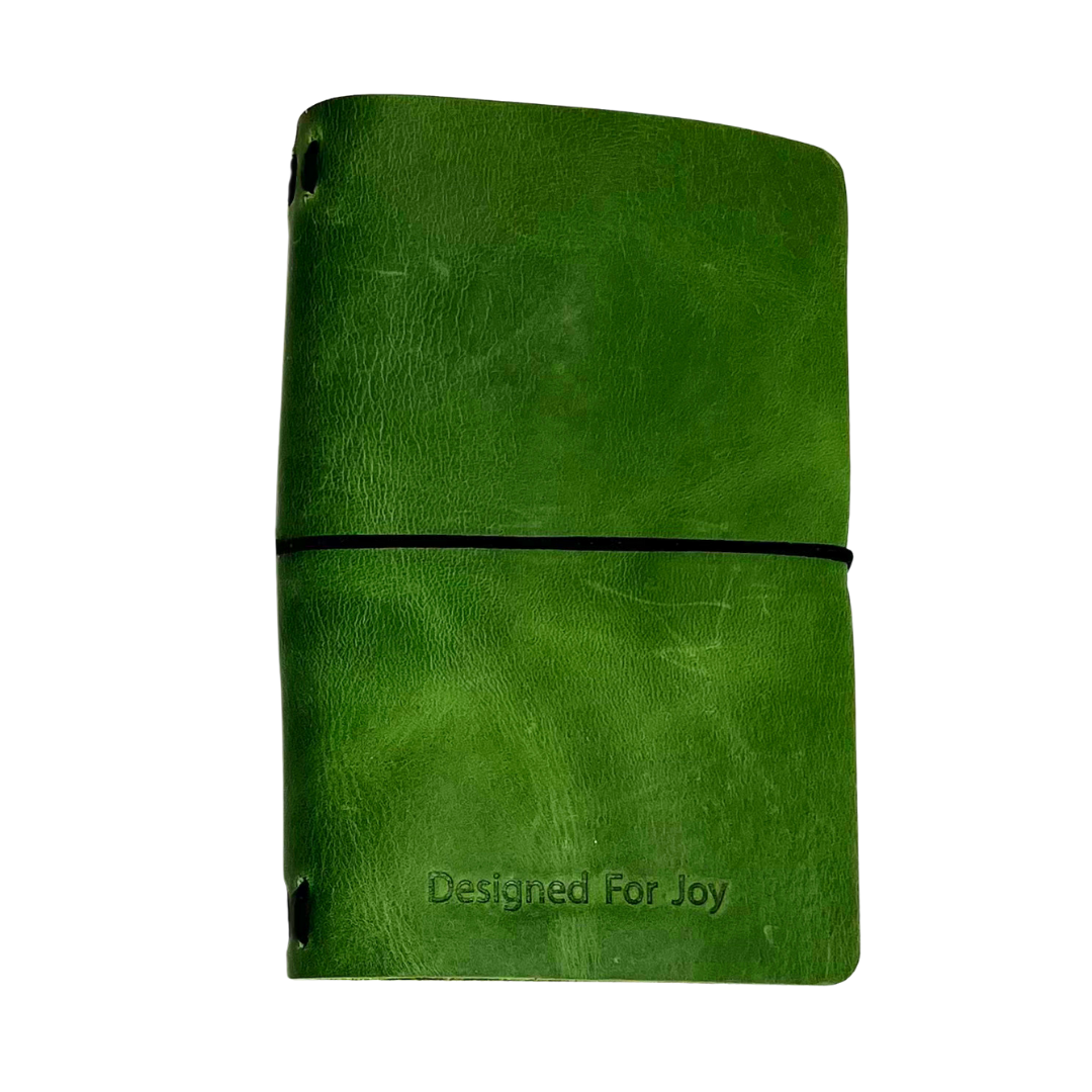 Green notebook with 'Designed for Joy' text on the cover and a black strap, on a white background