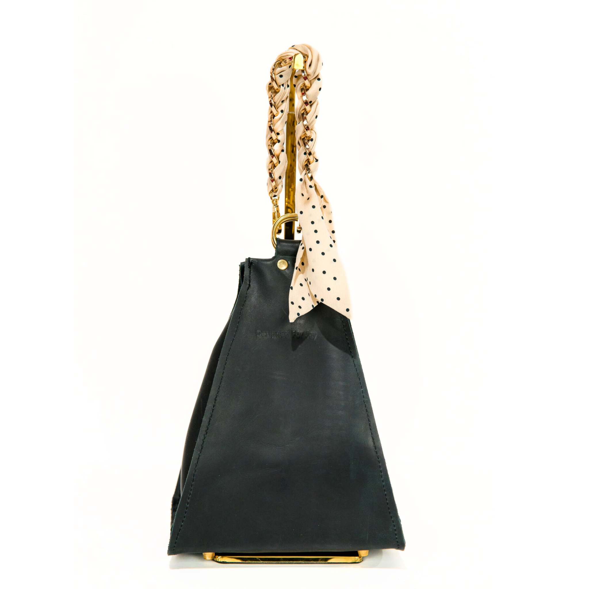 Black bucket handbag with a gold chain wrist strap that has a removable scarf and 'Designed for Joy' text, displayed on a white background
