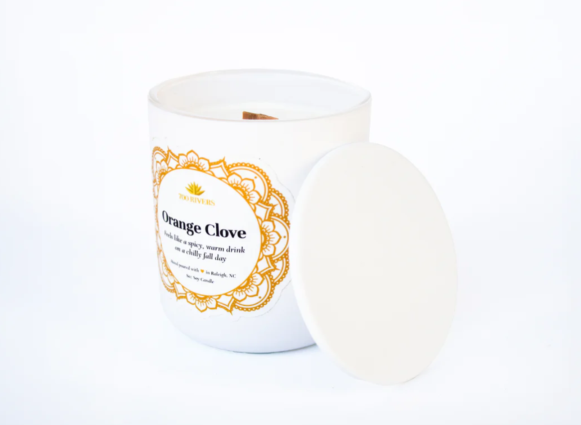 White candle with a wooden wick labeled 'Orange Clove' with orange floral designs