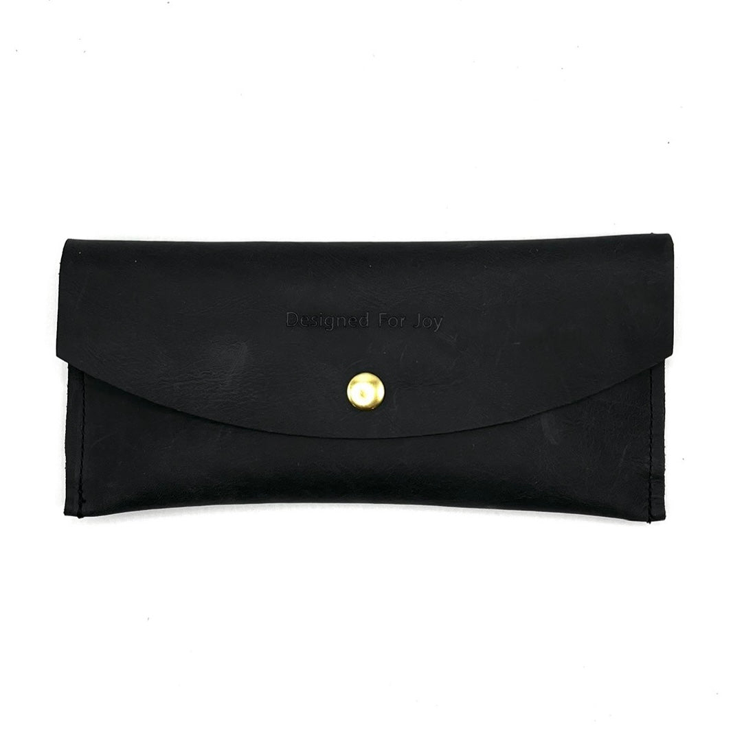 Black leather penny wallet with snap closure and 'Designed for Joy' text, displayed on a white background