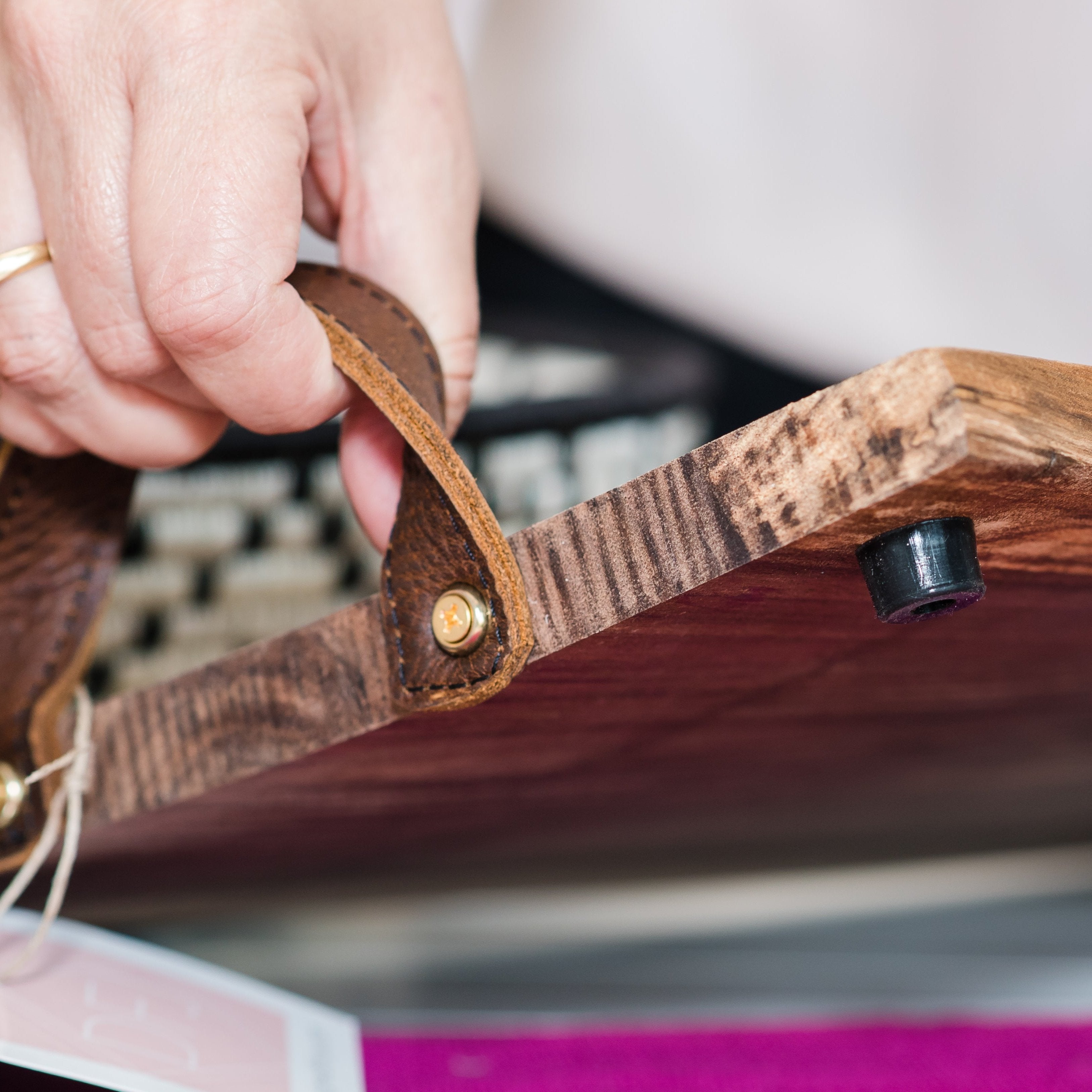 A close up of a person holding the leather handles of a charcuterie board