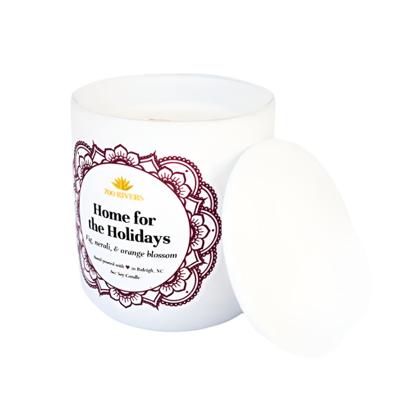 White candle with a wooden wick labeled 'Home for the Holidays' with purple floral designs