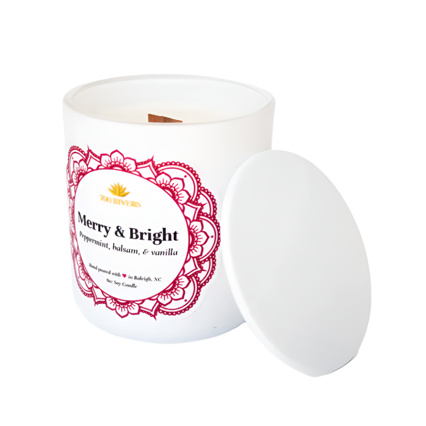 White candle with a wooden wick labeled 'Merry & Bright' with red floral designs