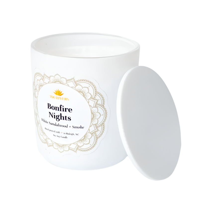 White candle with a wooden wick labeled 'Bonfire Nights' with white floral designs