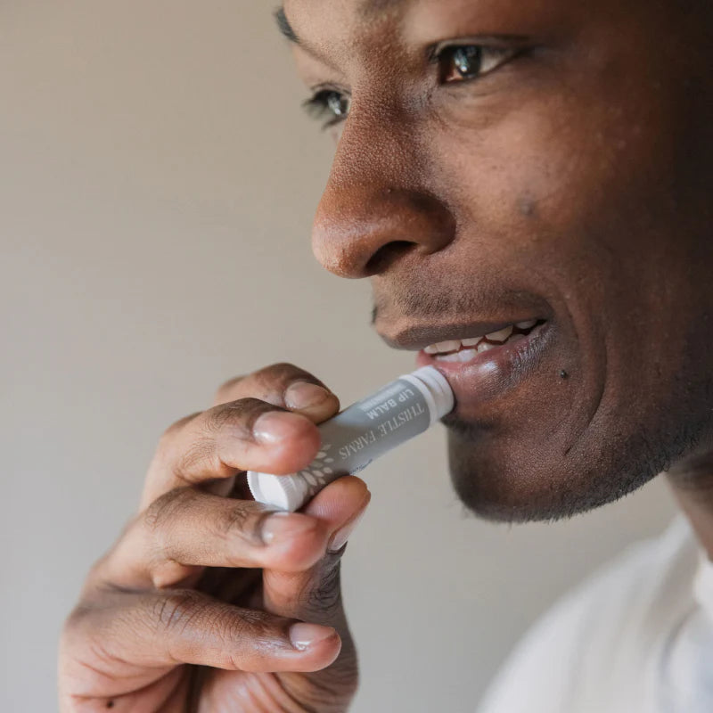 A close-up of a person putting on 'Thistle Farms Lip Balm Unscented'