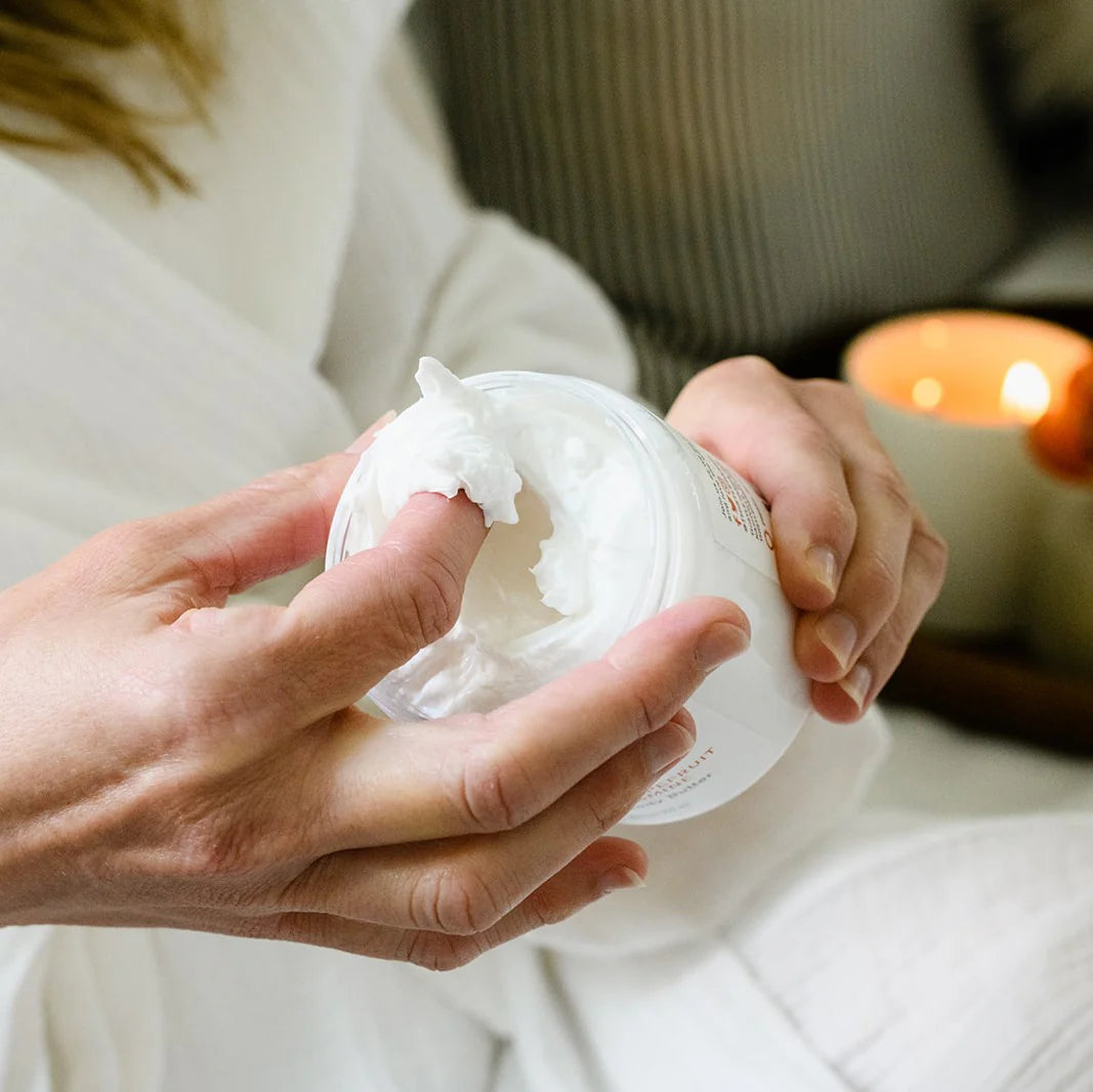 Close-up of a person scooping body butter with their fingers with a lit candle in the background