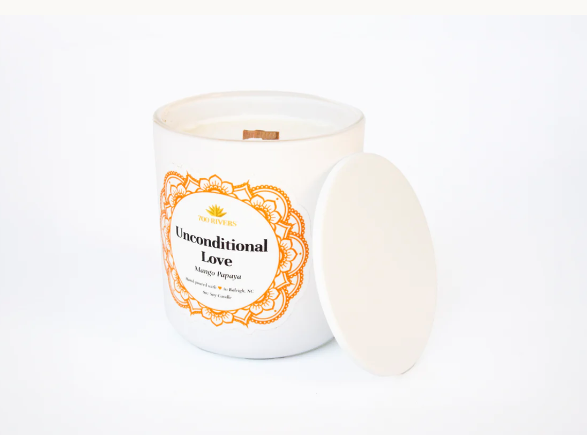 White candle with a wooden wick labeled 'Unconditional Love Mango Papaya' with orange floral designs