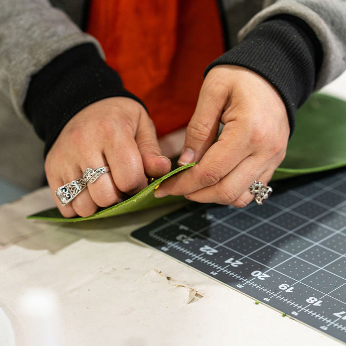 A pair of hands working on a green craft material on a measuring board