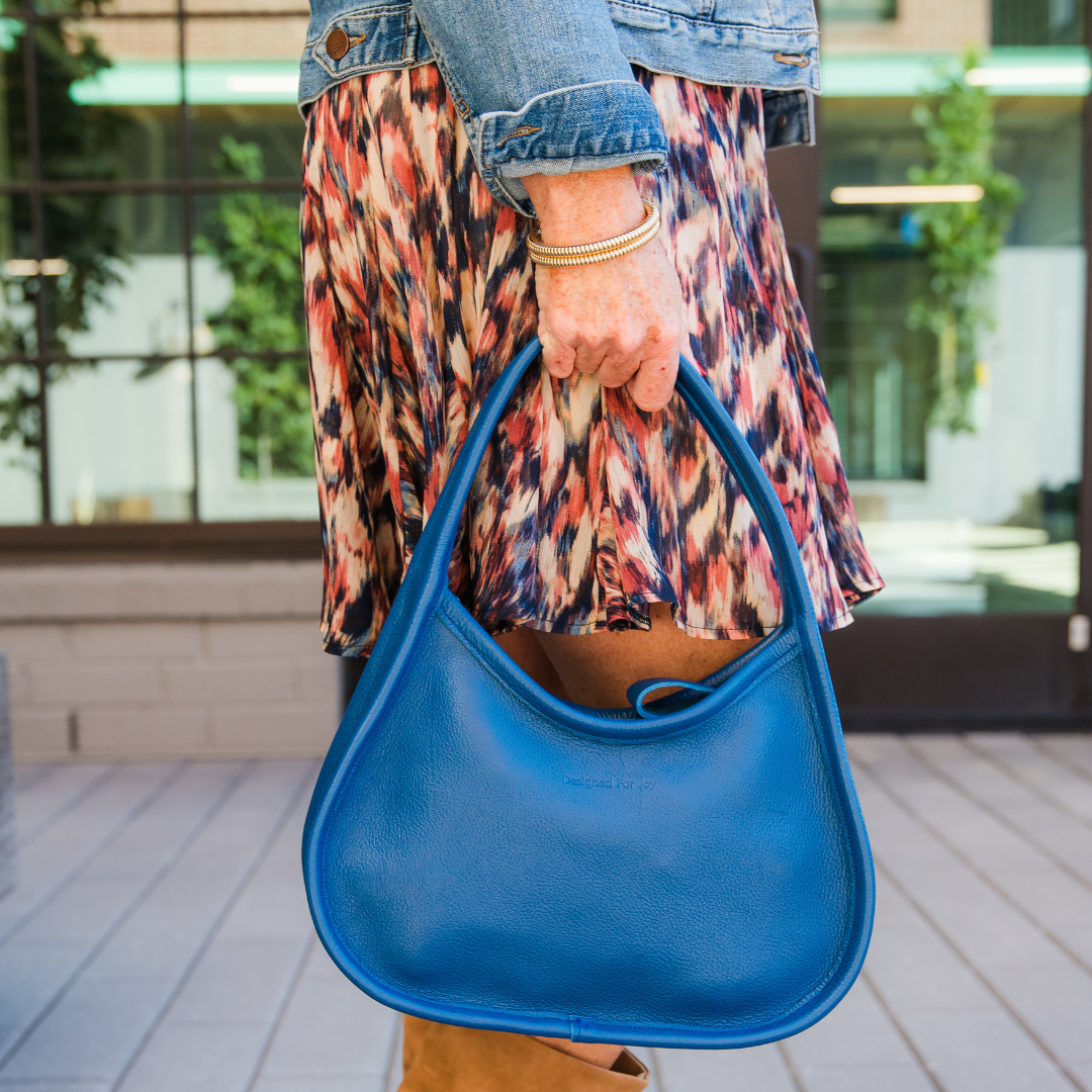 Close-up of a person holding a blue shoulder handbag in an outdoor setting