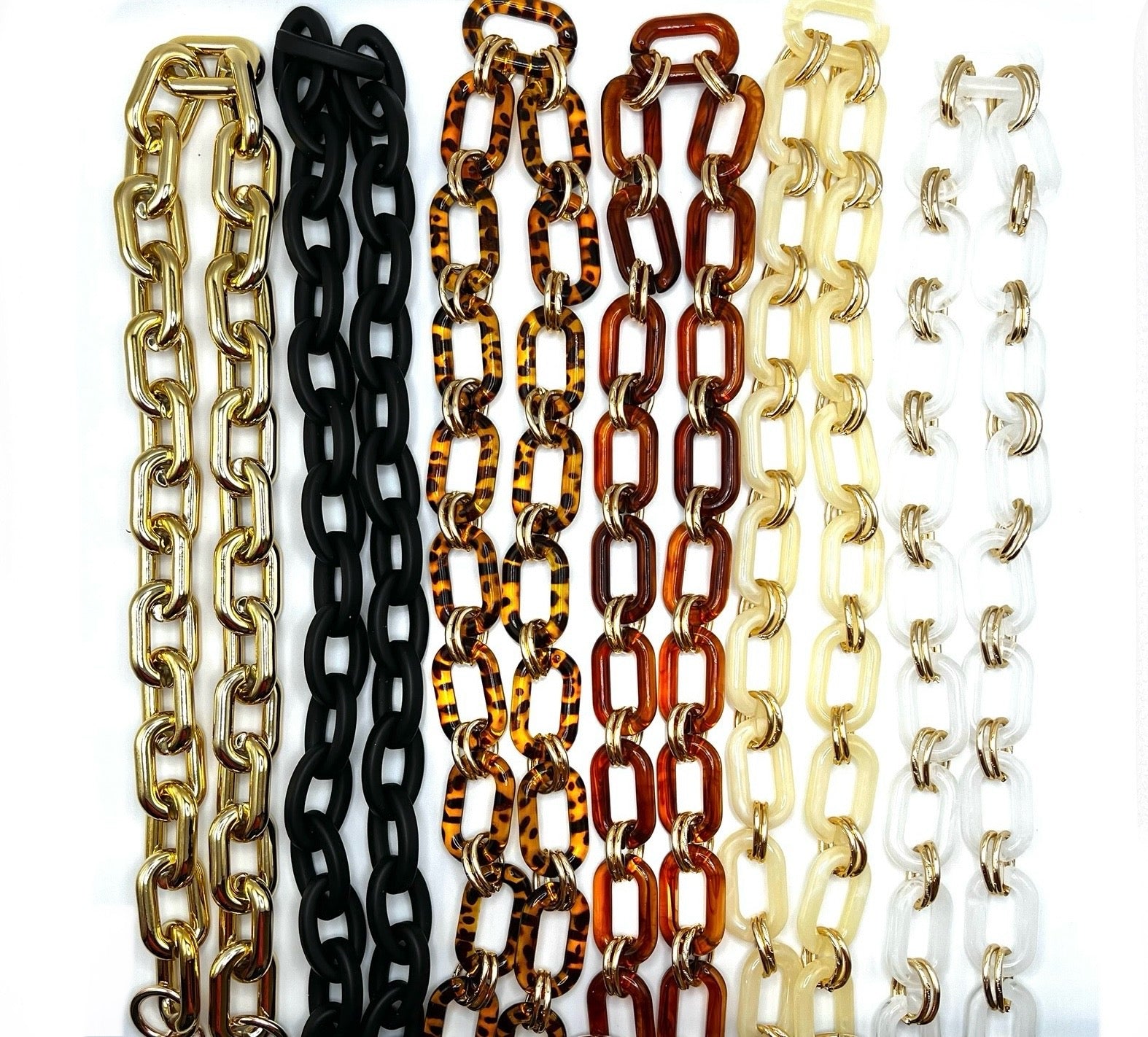 Collection of acrylic chain straps in various colors, including gold, black, tortoise shell, amber, cream, and white with gold accents and clips