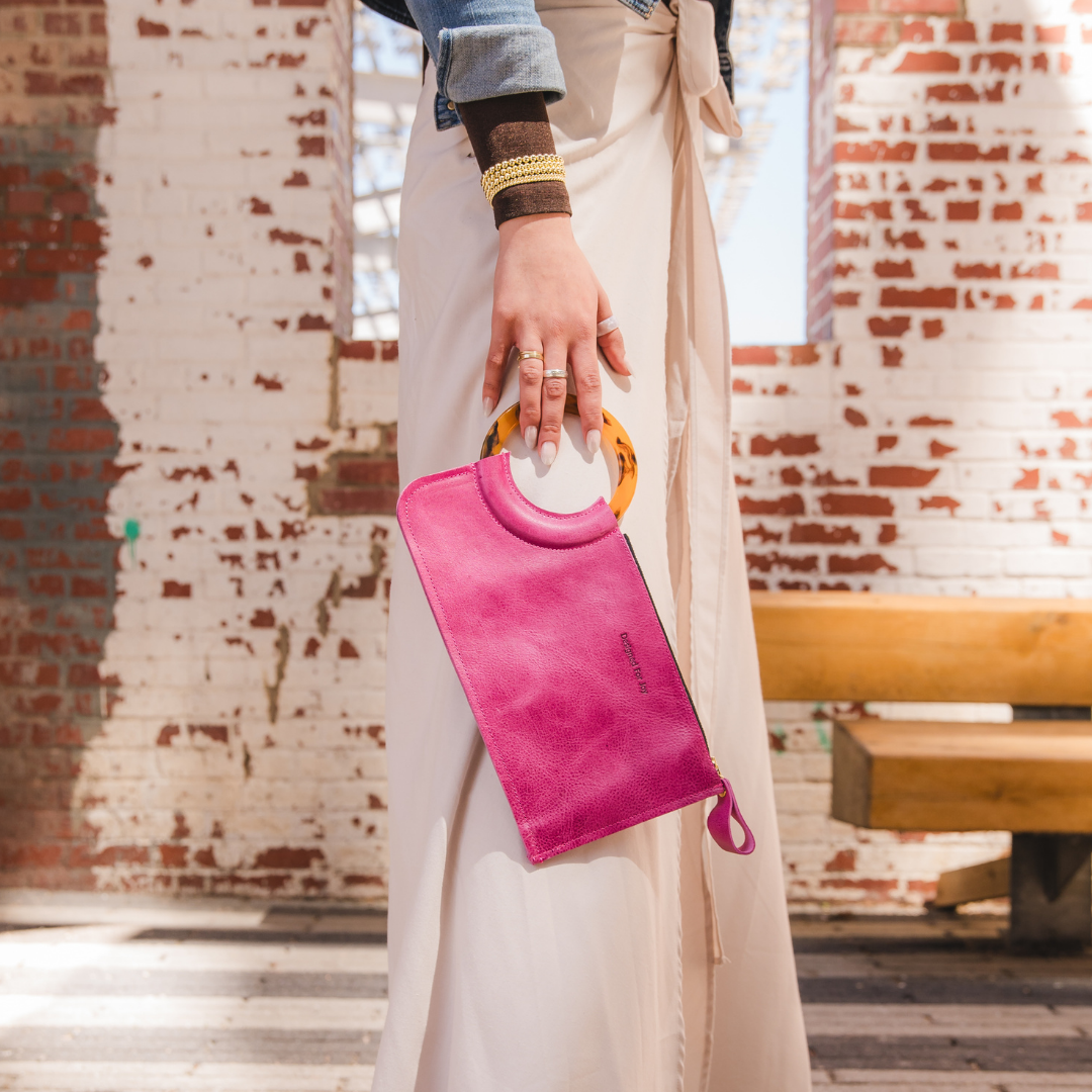 A person standing sideways holding a pink wristlet handbag