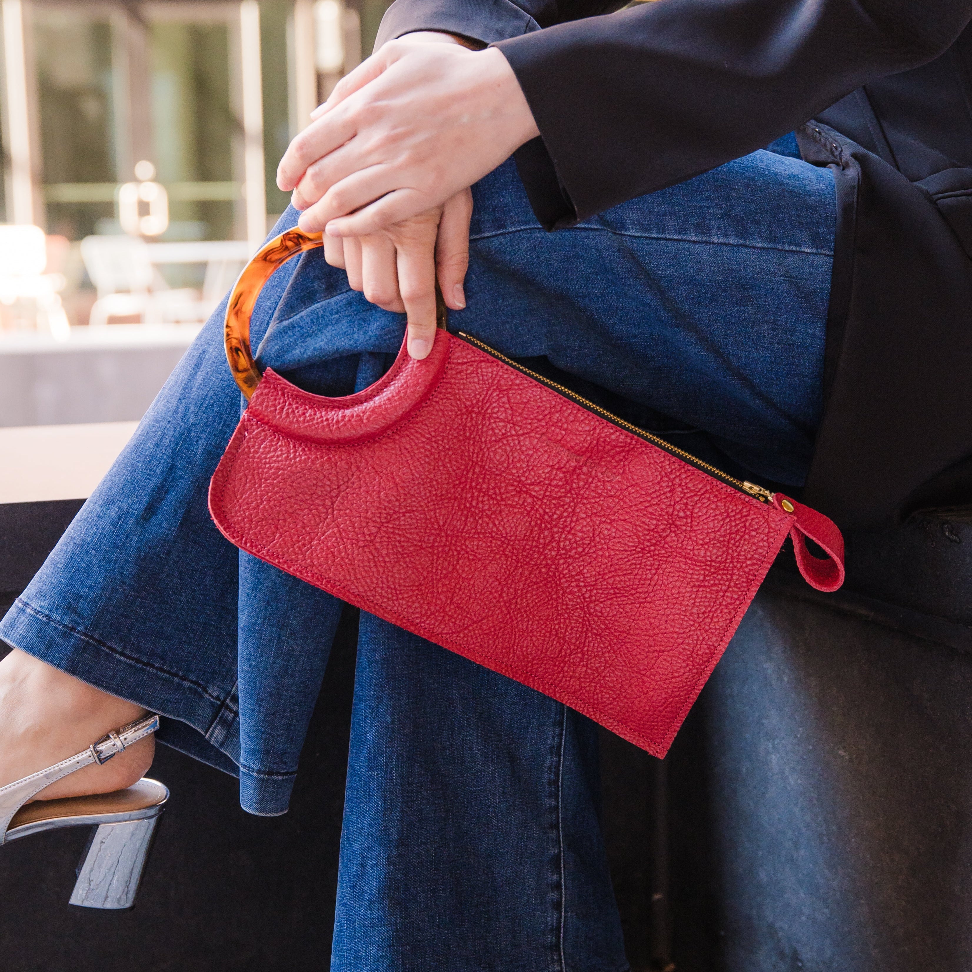 Person holding a red wristlet handbag against their crossed legs