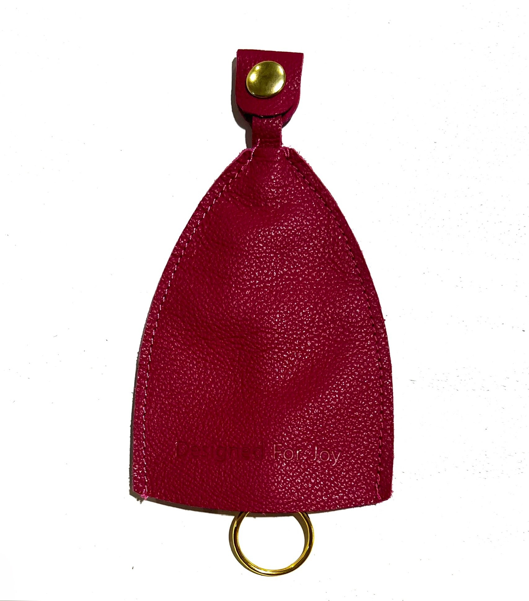 Pink leather car key cover with 'Designed for Joy' text and a gold metal ring peeking out of the bottom, on a white background