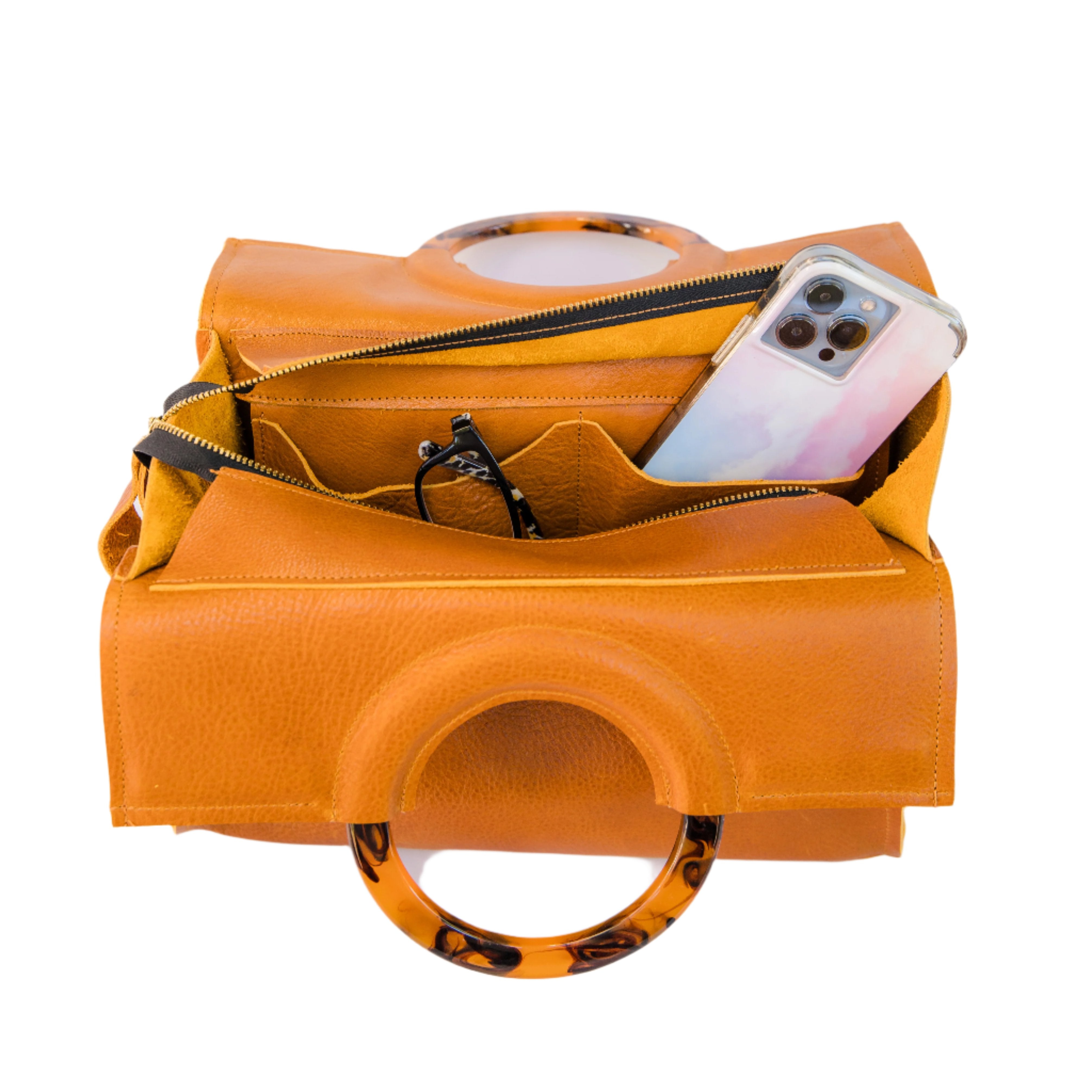 Overhead shot of an open caramel brown satchel handbag showcasing pockets with a phone and sunglasses in it, displayed on a white background