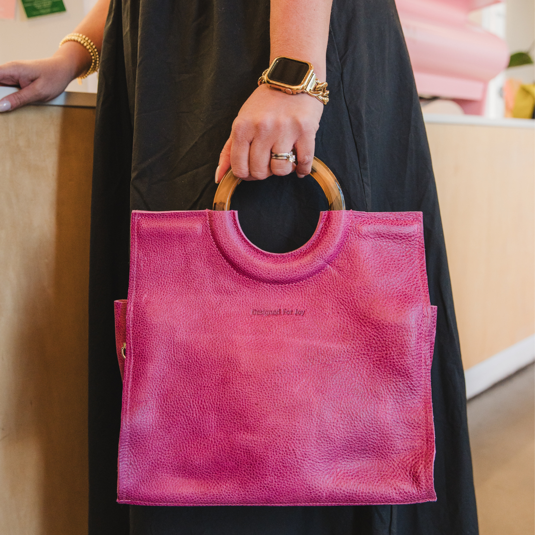 Close-up of a person holding a pink satchel handbag in an indoor setting