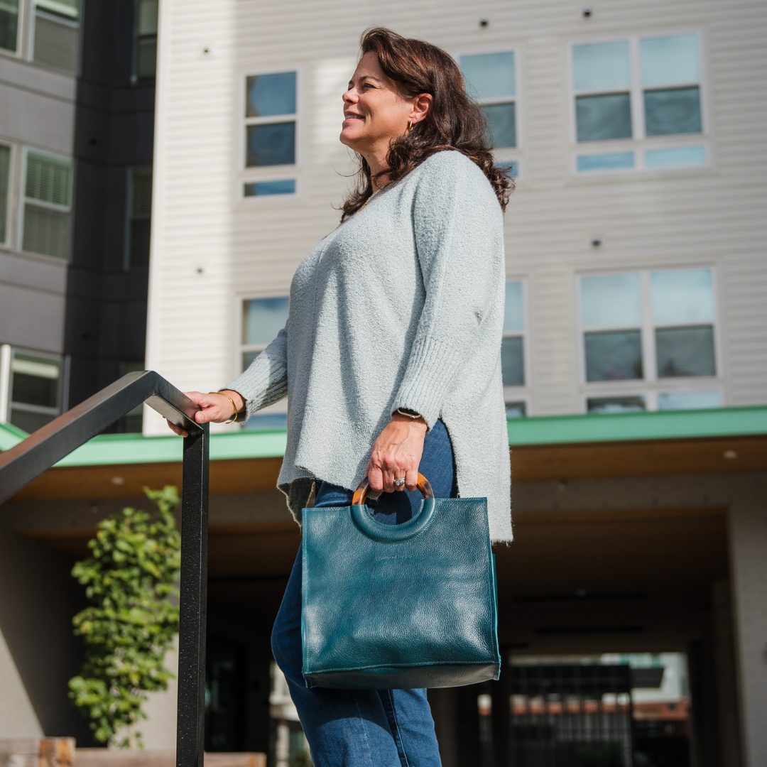 Person holding a teal satchel handbag while standing on stairs in an outdoor setting