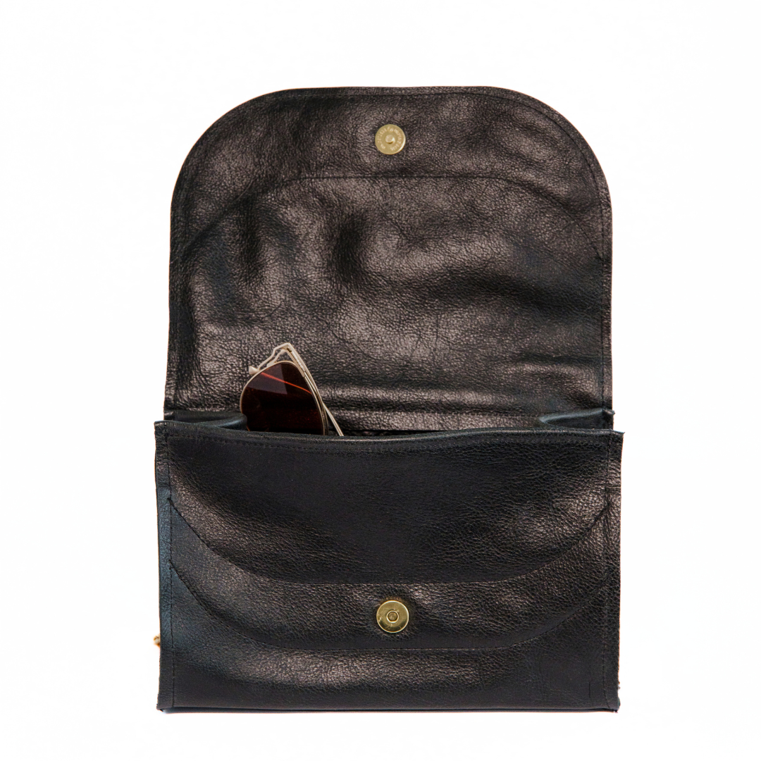 Open black pebbled leather shoulder handbag with glasses peeking out of pocket, on a white background