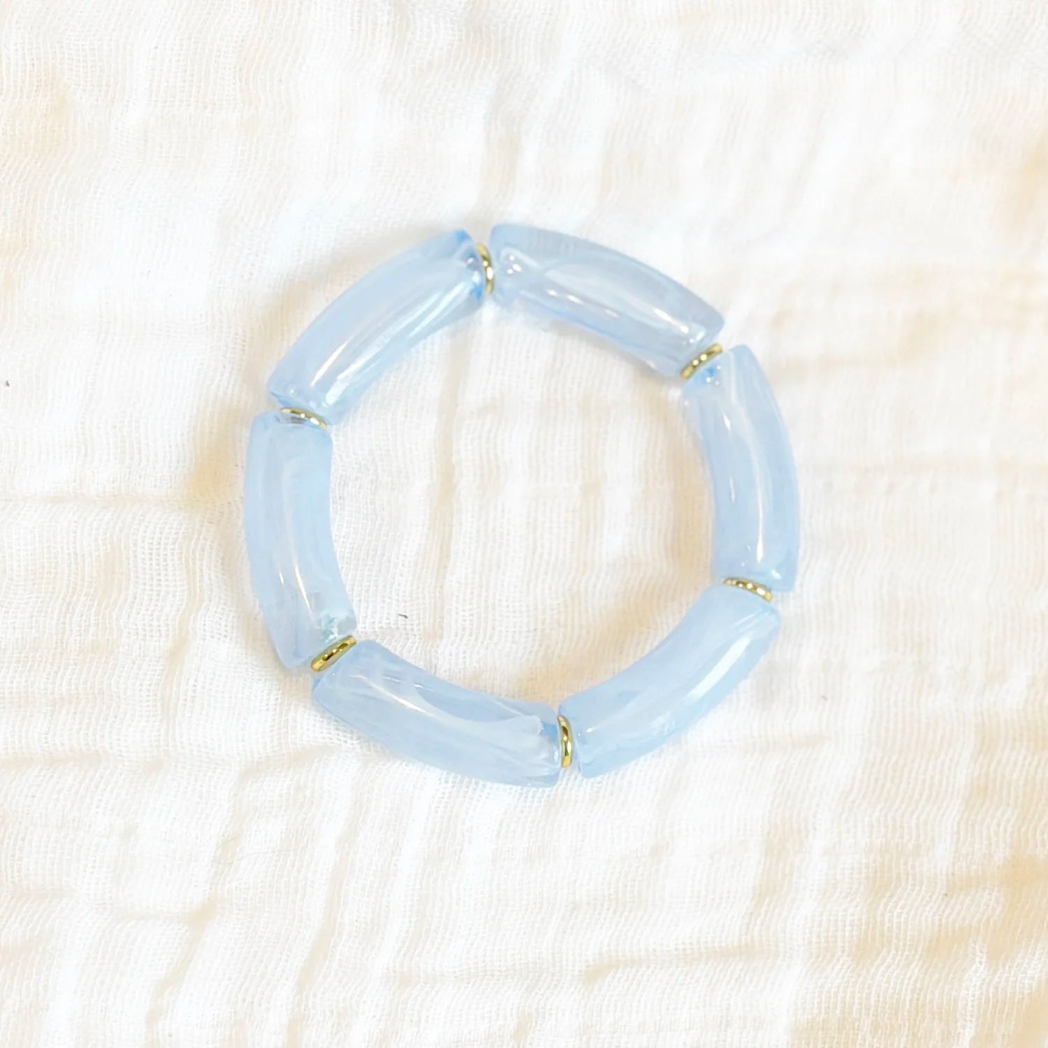 Bracelet featuring blue acrylic beads with gold spacers, displayed on a white fabric background