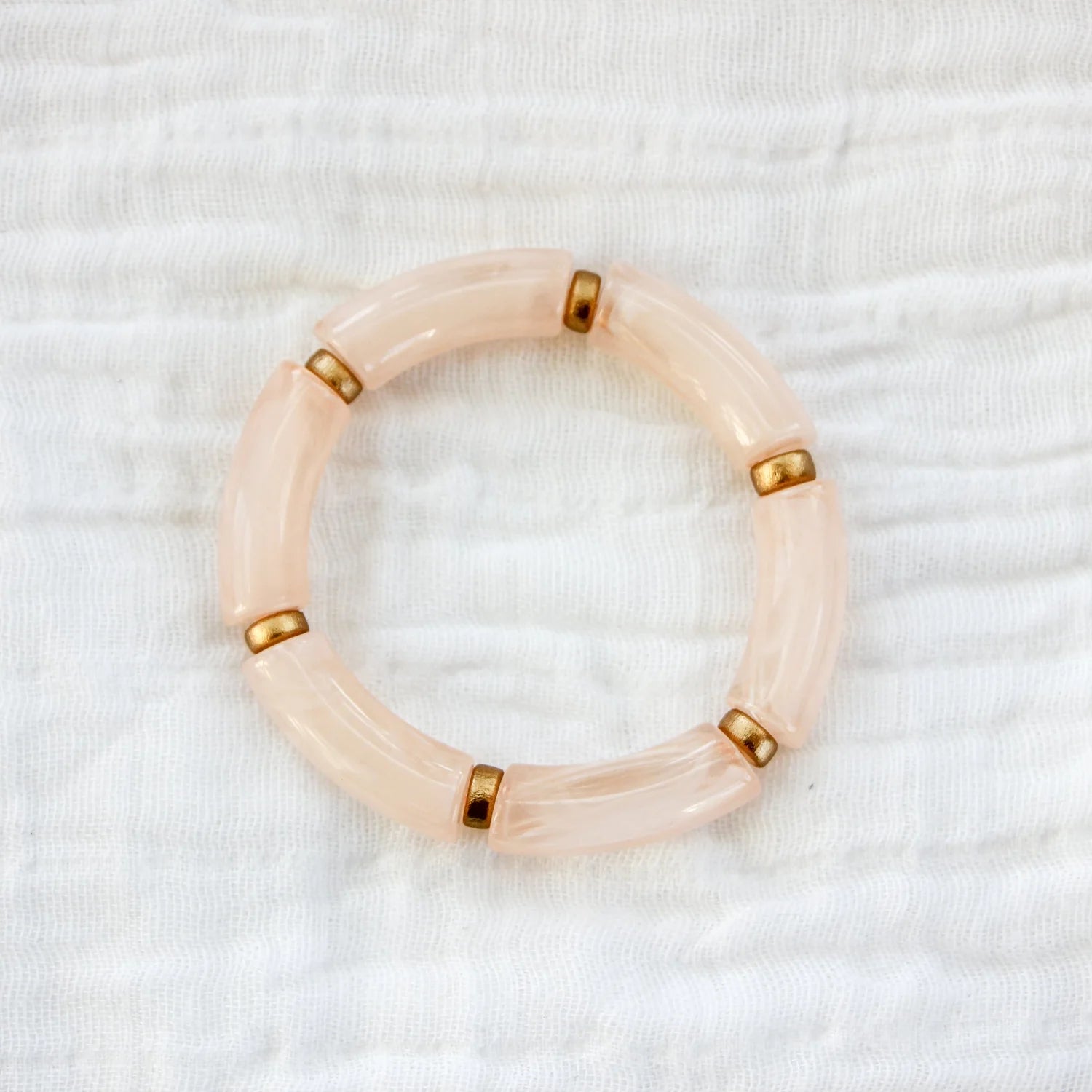 Bracelet featuring blush pink acrylic beads with gold spacers, displayed on a white fabric background