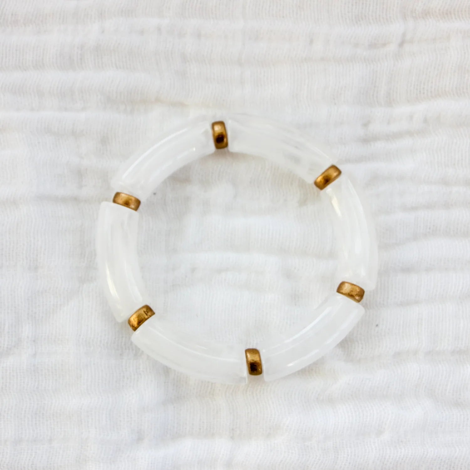 Bracelet featuring white acrylic beads with gold spacers, displayed on a white fabric background