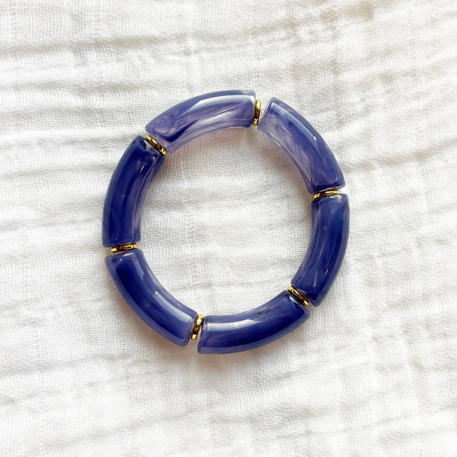 Bracelet featuring purple acrylic beads with gold spacers, displayed on a white fabric background