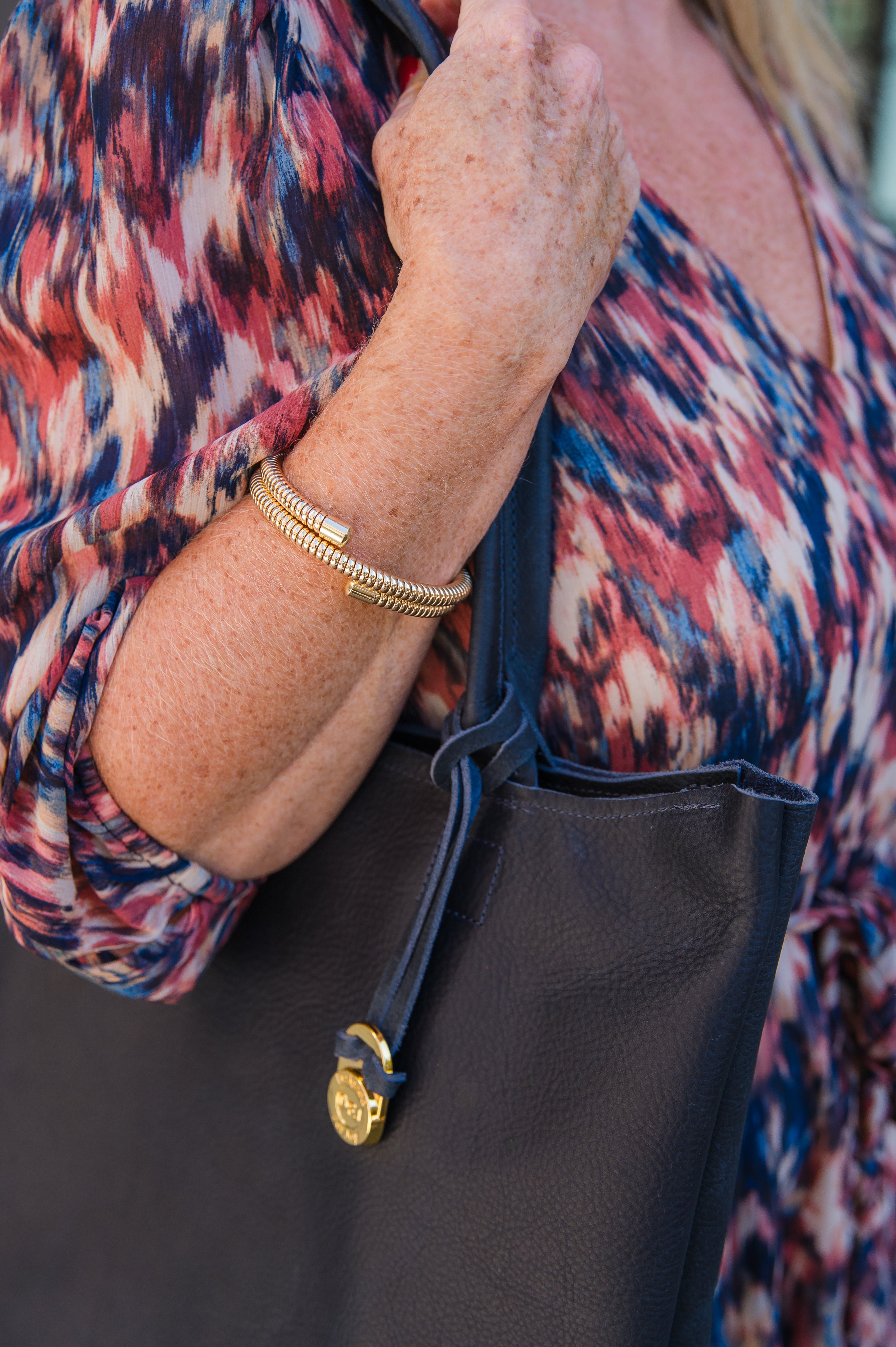 Close up of a person wearing the gold coil bangle bracelet while holding a bag
