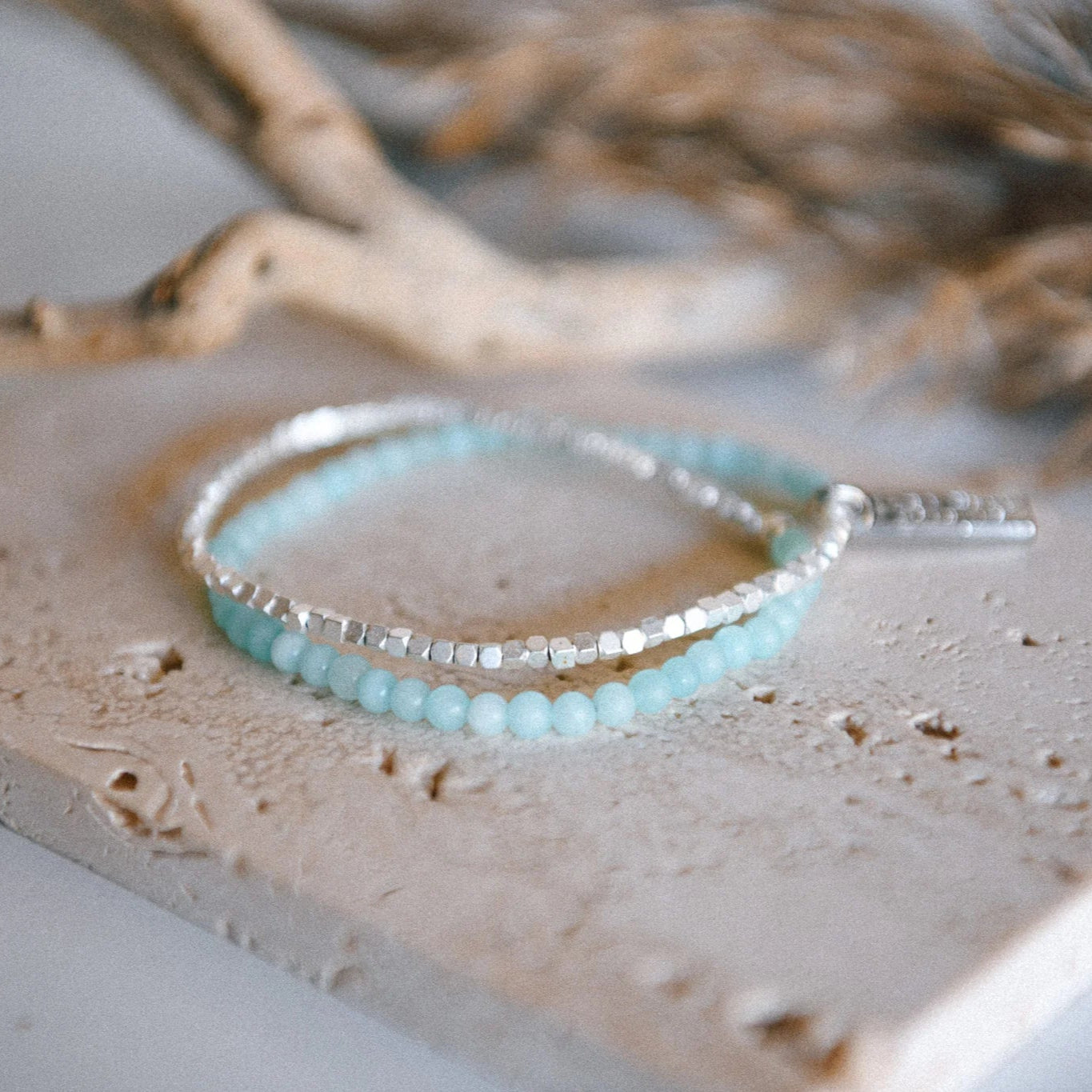 A half jade, half matte silver-colored beaded bracelet on a stone surface with a blurred background