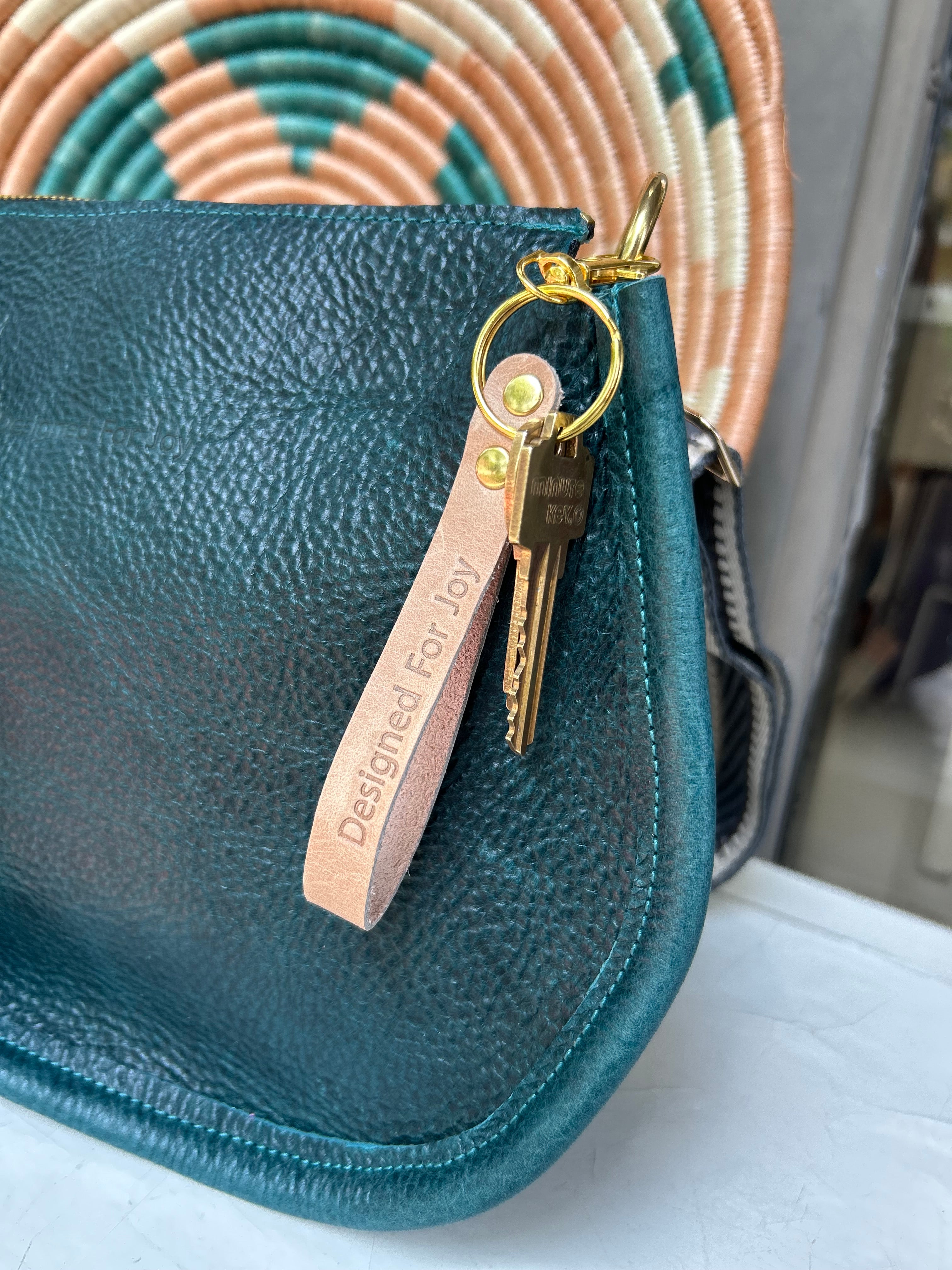 Brown keychain with keys and leather tag with 'Designed for Joy' text on a blue bag
