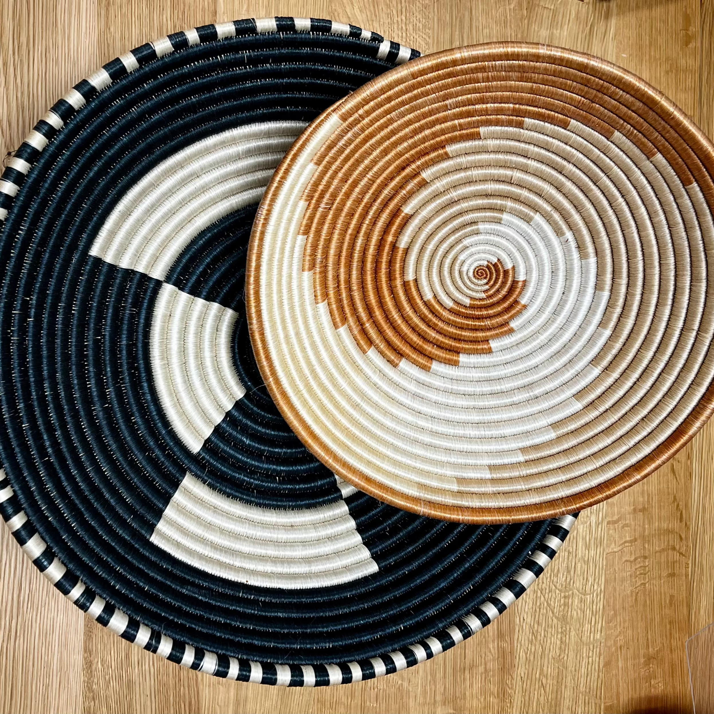 Two Rwandan baskets, one navy and white and the other brown and white, displayed on a wooden surface