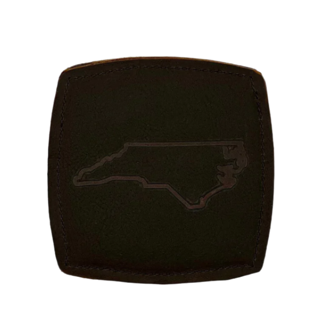 Brown leather coaster with an NC state outline stamped in the center, displayed on a white background