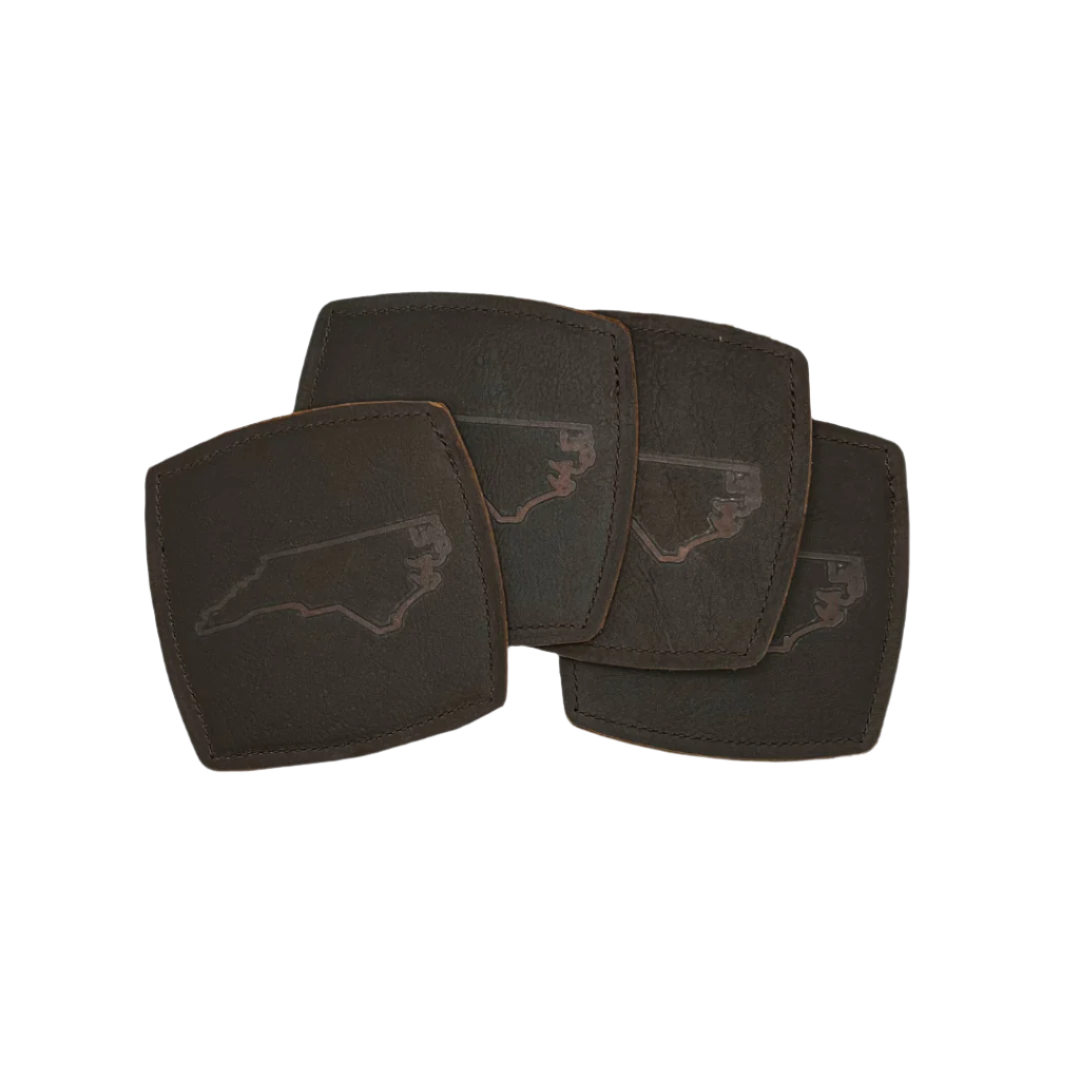 A set of four square brown leather coasters with an NC state outline stamped in the center, displayed on a white background